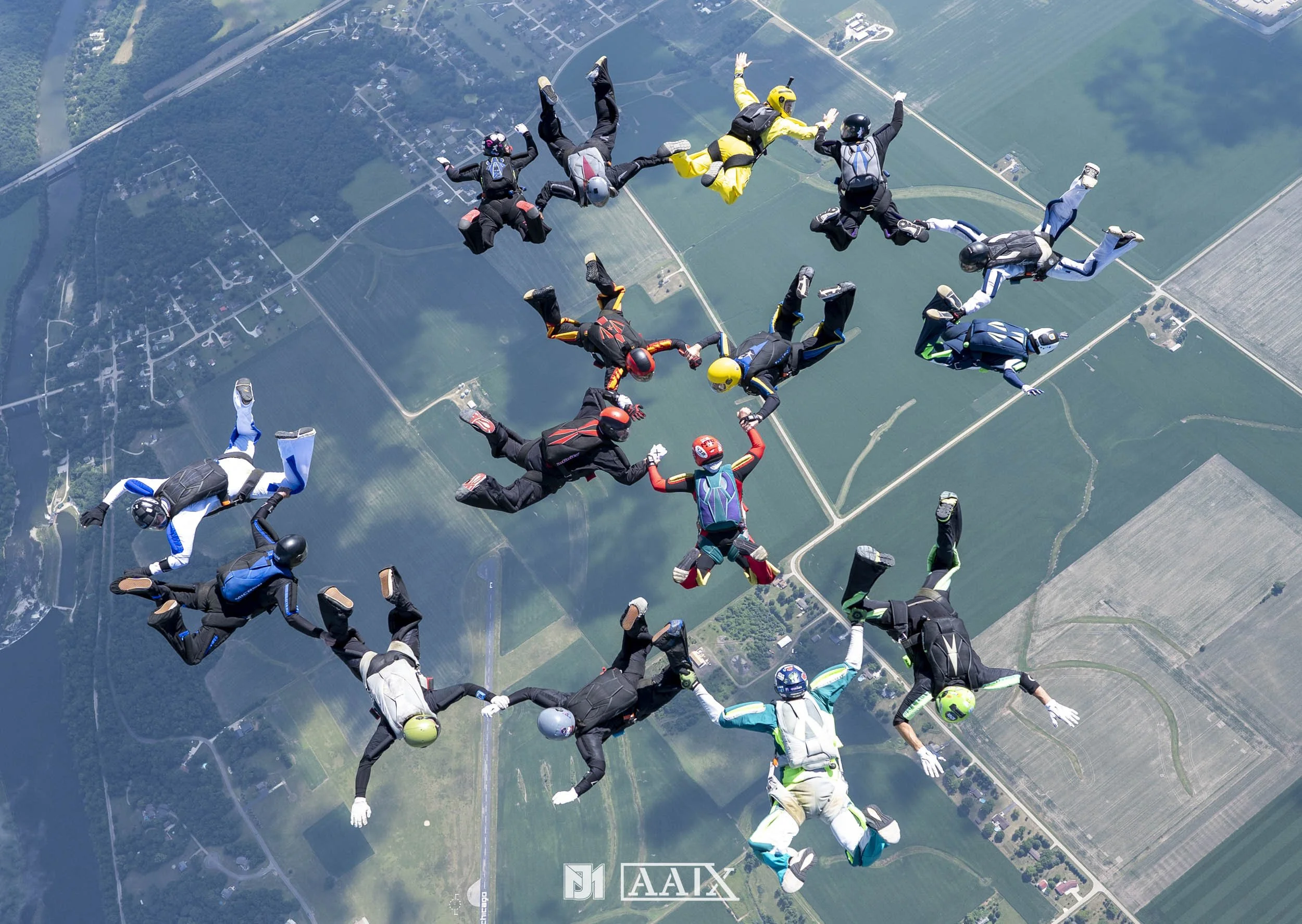 Group of skydivers in freefall formation over green fields and farmland.