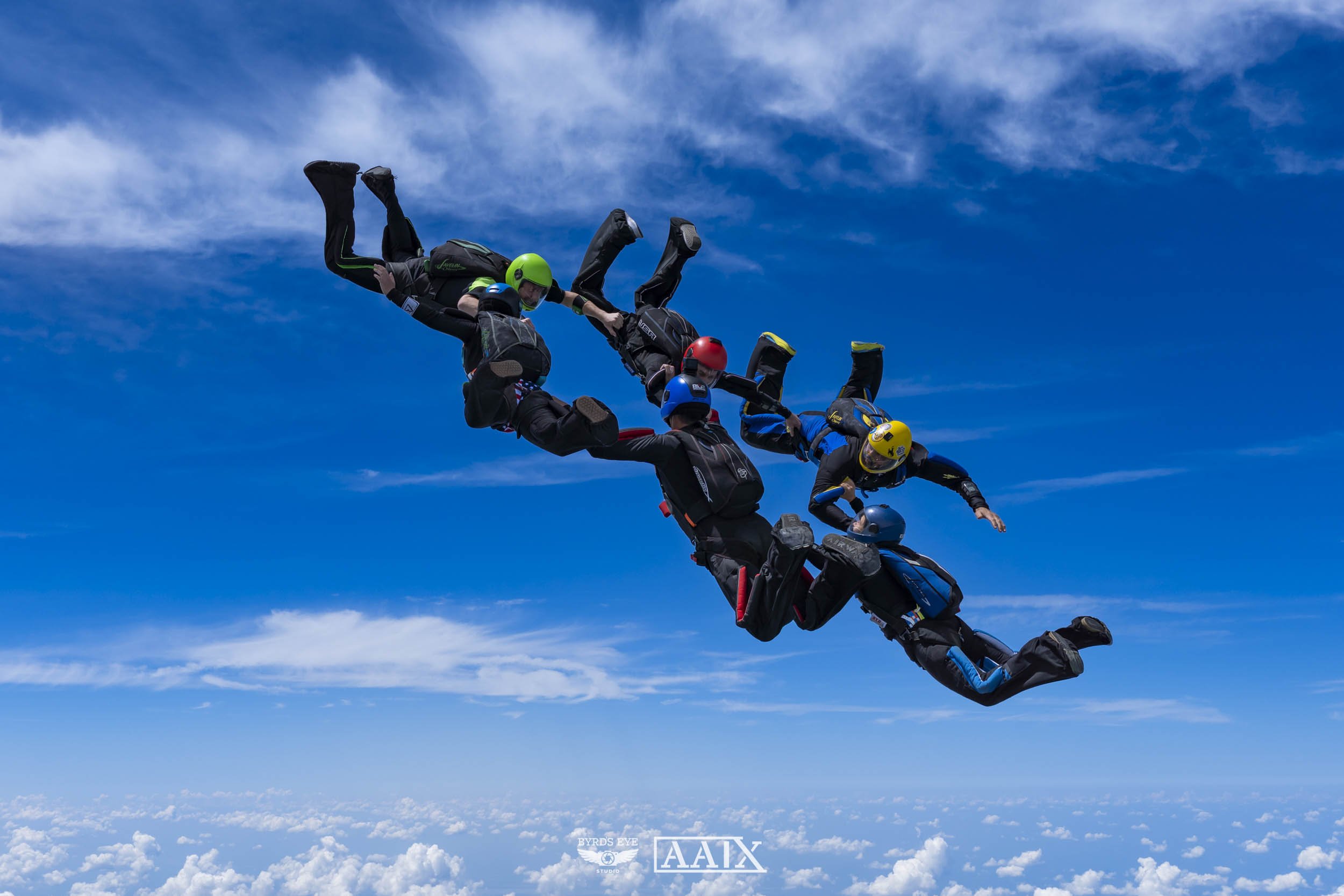 Skydivers holding hands in a circle mid-air against blue sky and clouds