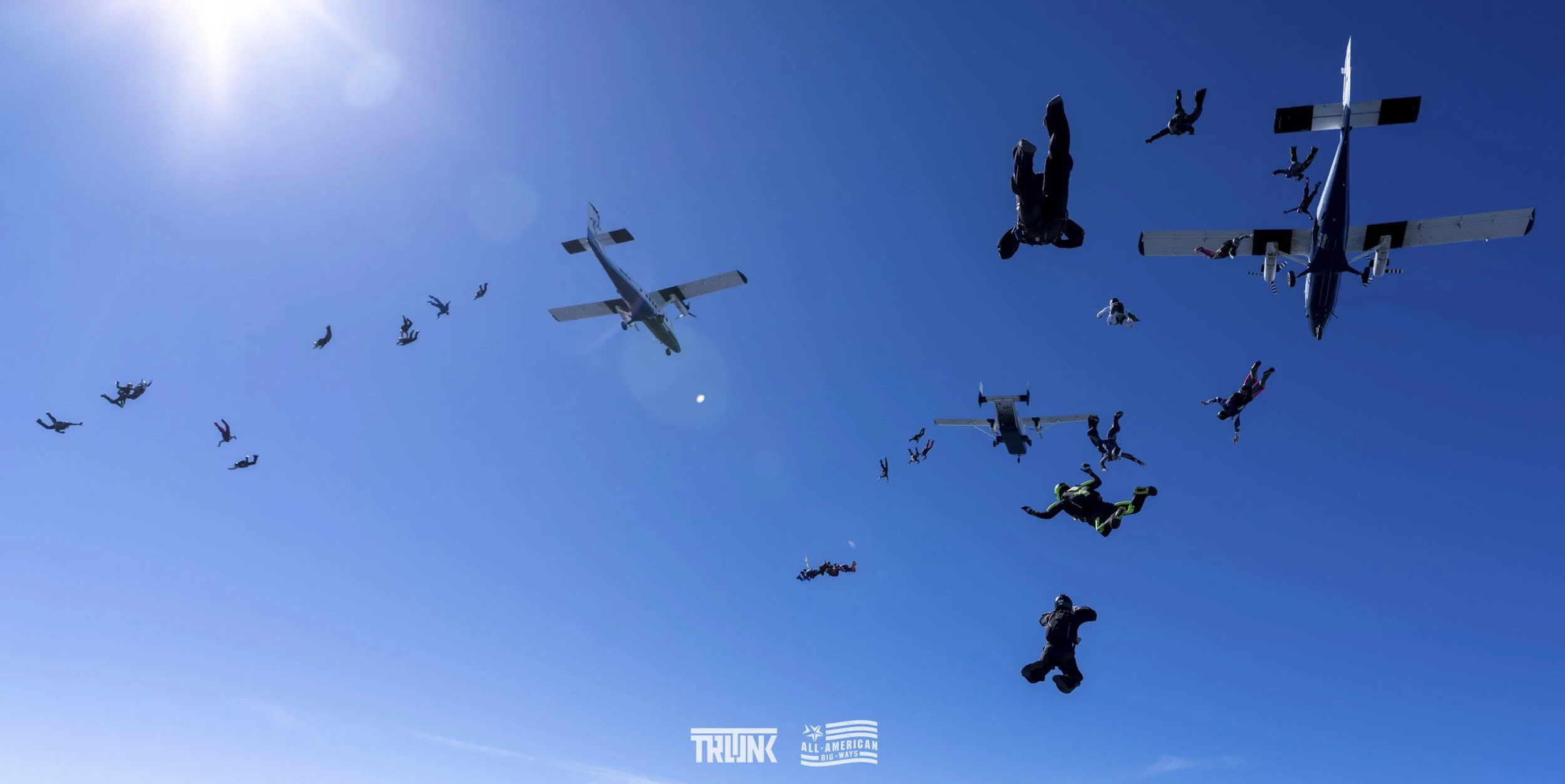 Skydivers free-falling from airplanes against a bright blue sky.