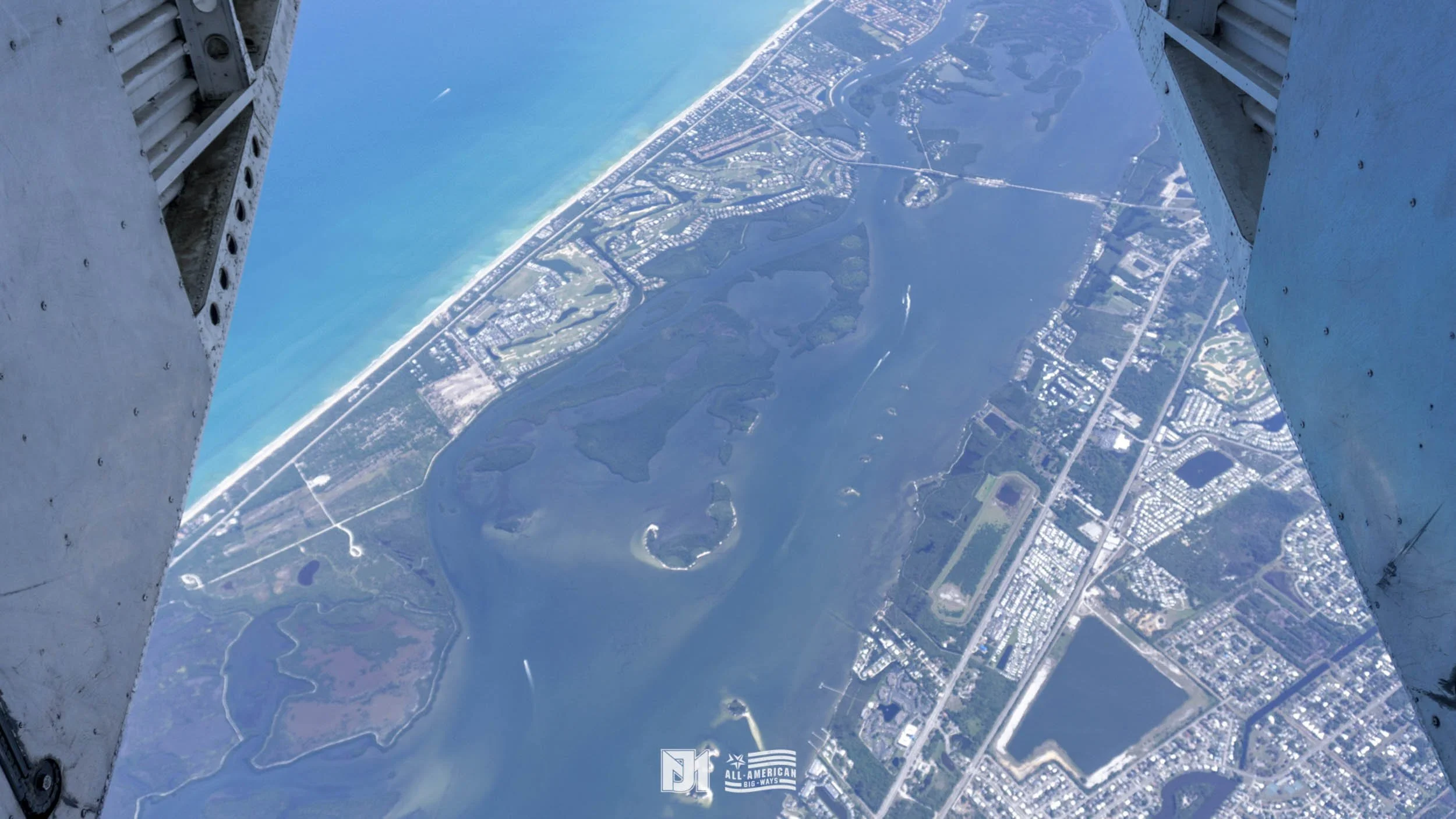 Aerial view of a coastal city with lakes, roads, and residential areas, seen from an aircraft in flight.