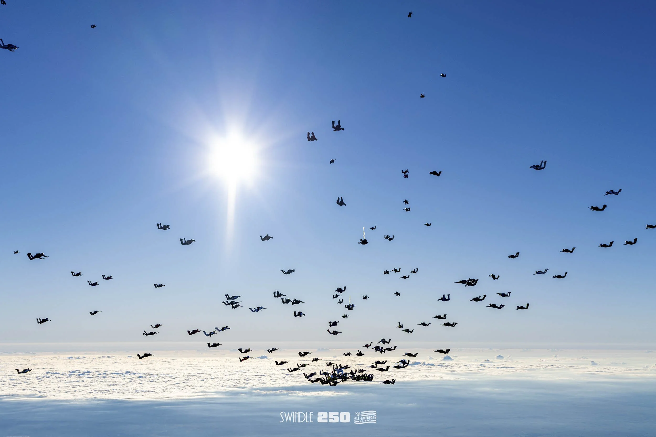 A group of skydivers jumping from an airplane in a clear blue sky with the sun shining brightly and snow-covered ground below.