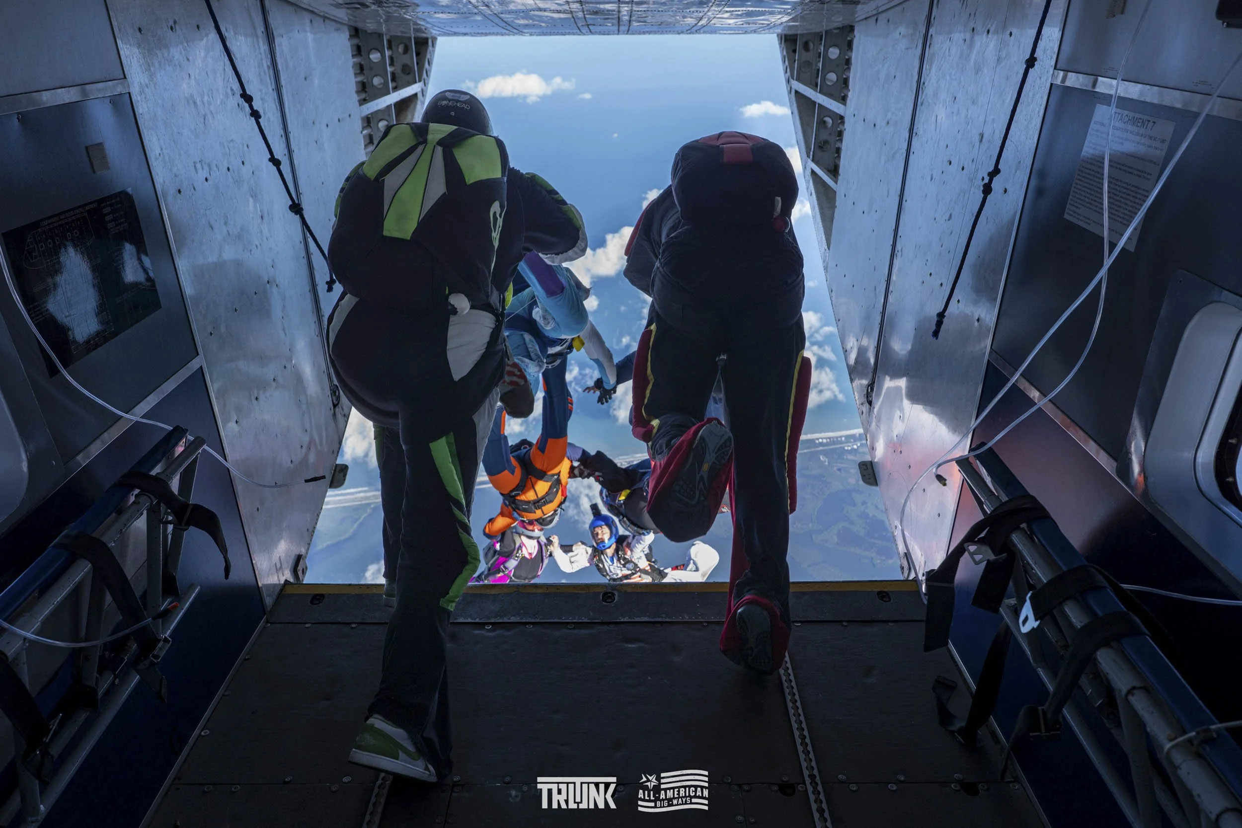 Skydivers preparing to jump from a plane with a view of clouds and landscape below.