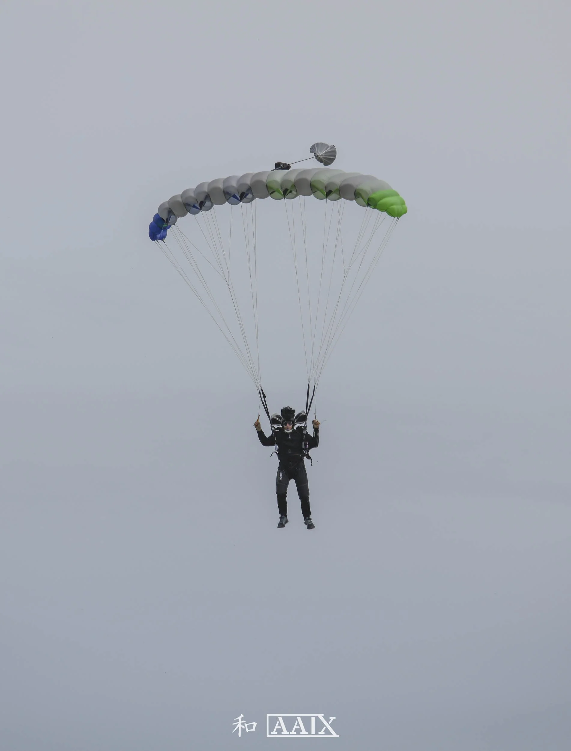 A person skydiving with a parachute against a cloudy sky, with Japanese characters and Greek letters on the bottom.