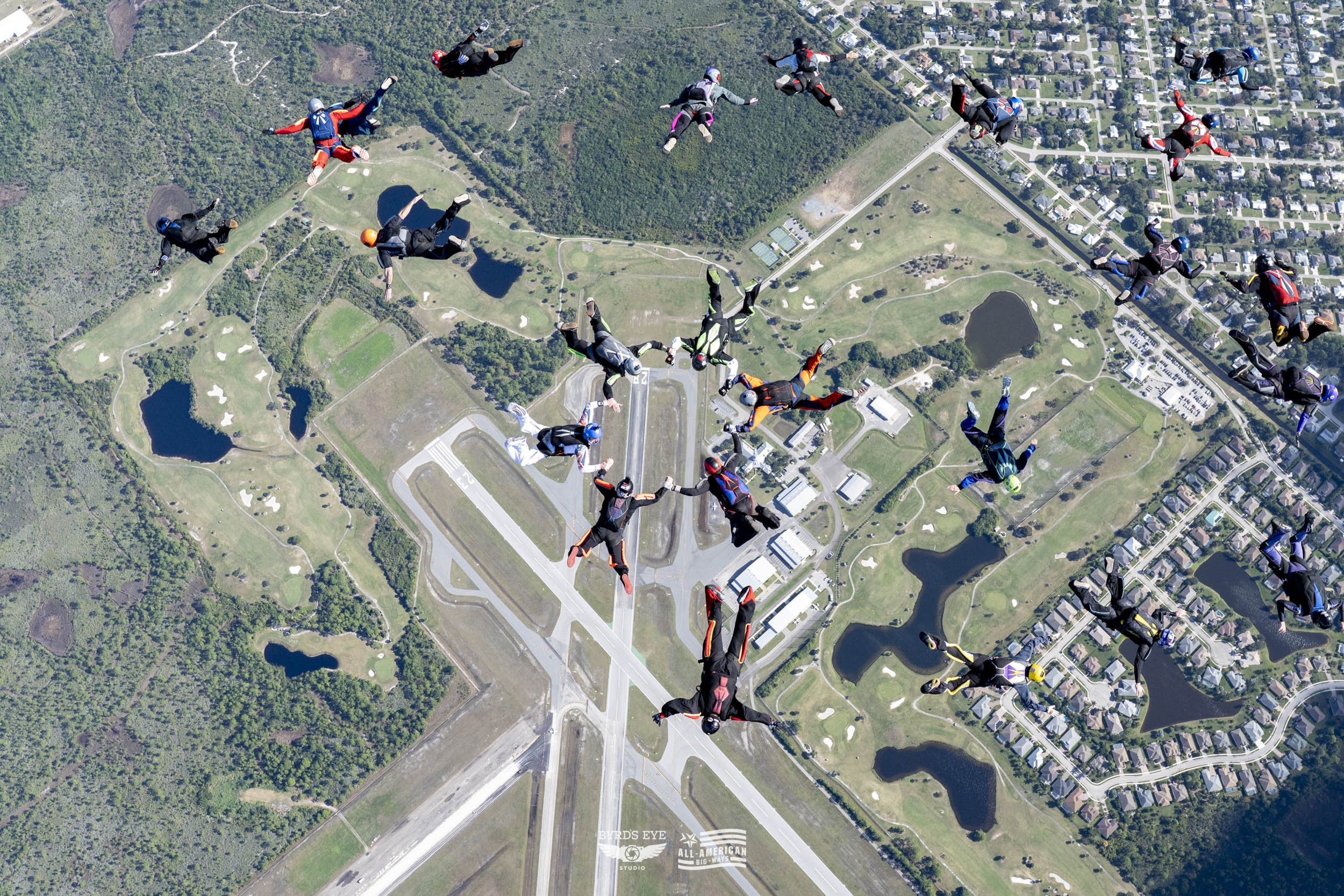 Group of skydivers in free fall above a landscape of lakes, trees, roads, and residential neighborhoods
