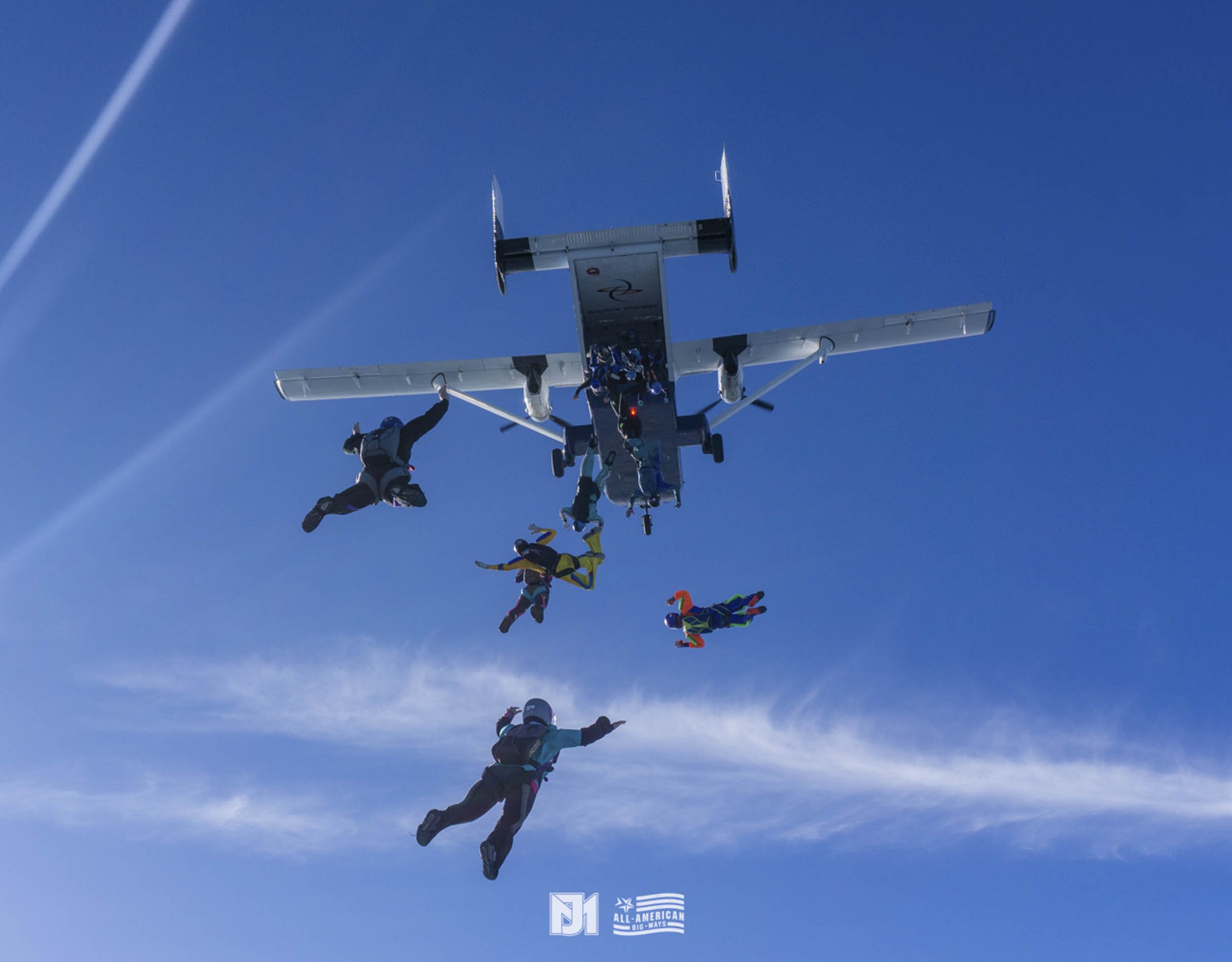 Skydivers mid-air jumping away from a small airplane against a clear blue sky