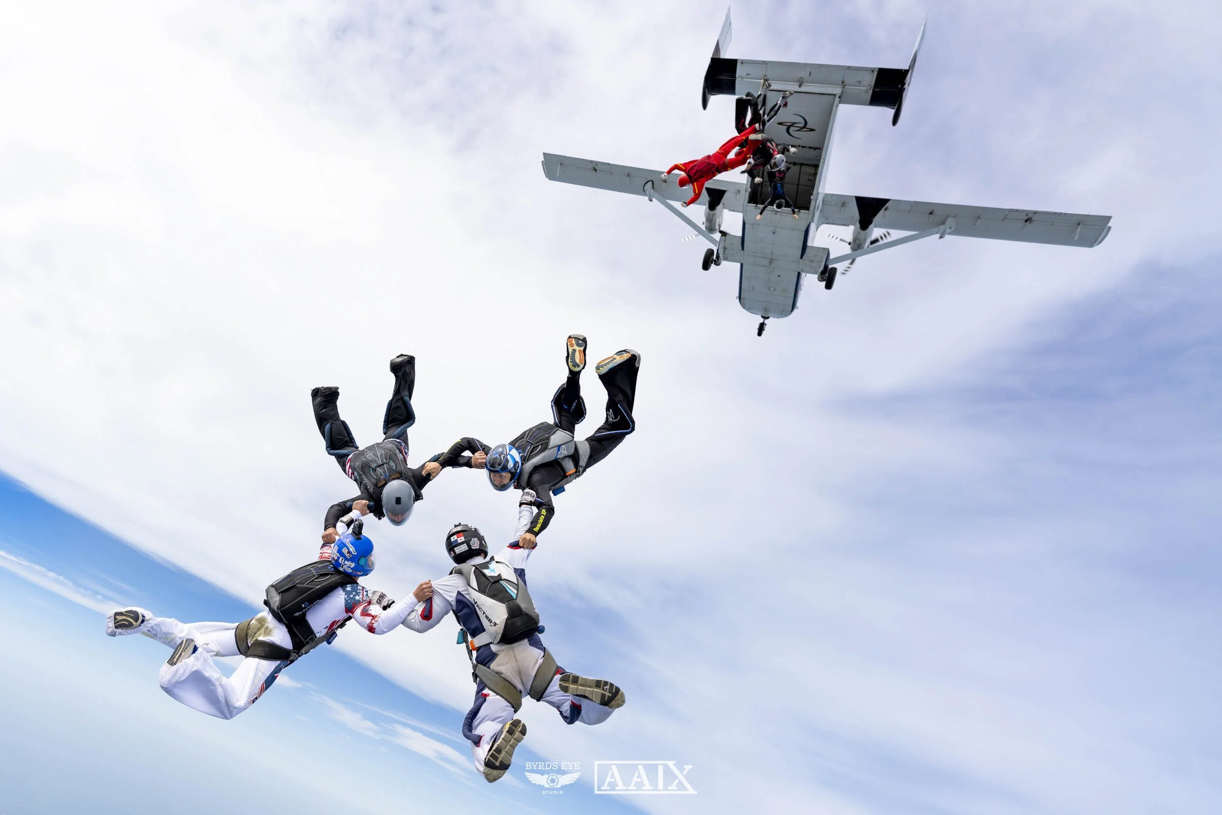 A group of skydivers holding hands in a circle while free-falling from an airplane in the sky.