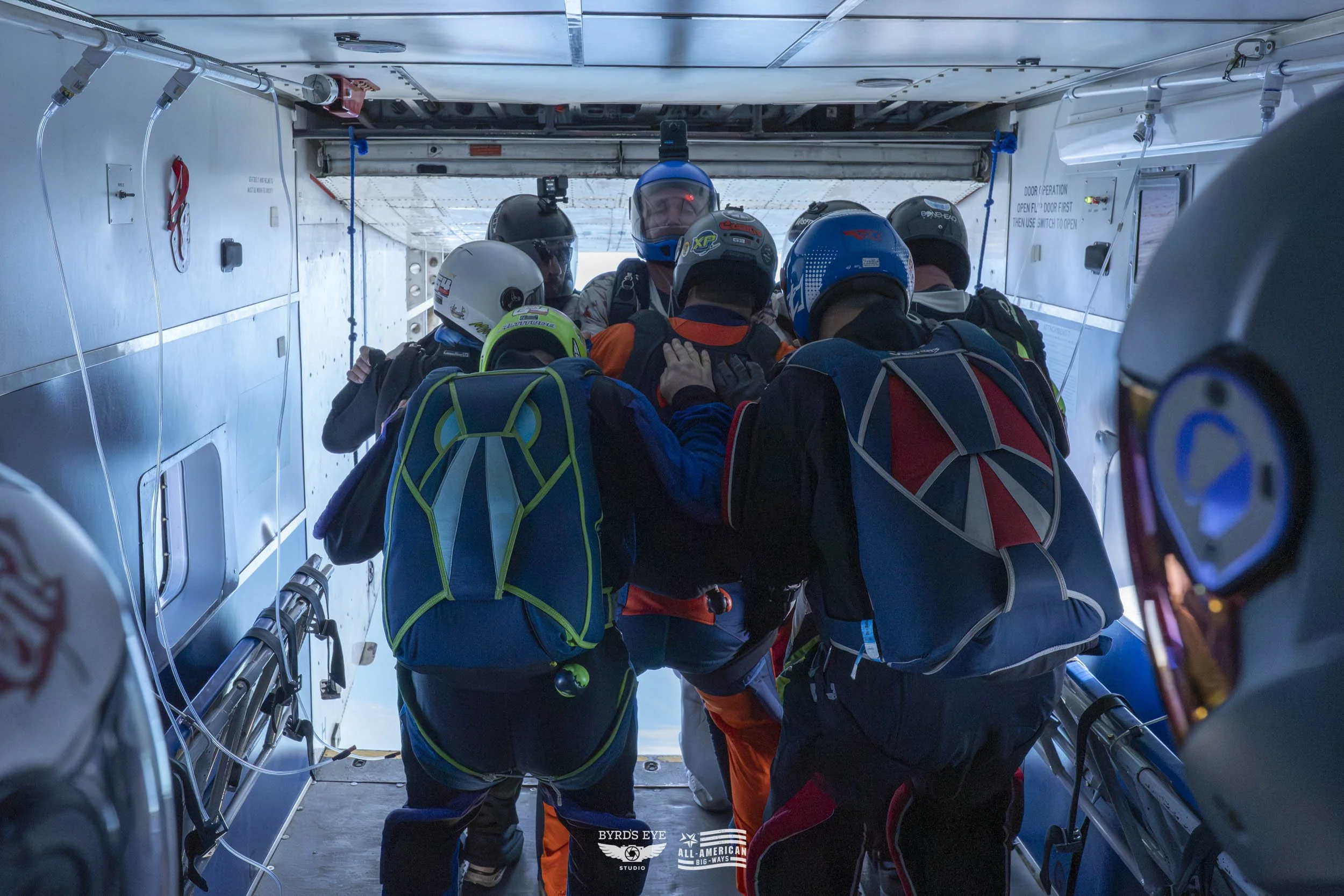 A group of skydivers in helmets and jumpsuits preparing to jump from an aircraft, crowded near the open door.