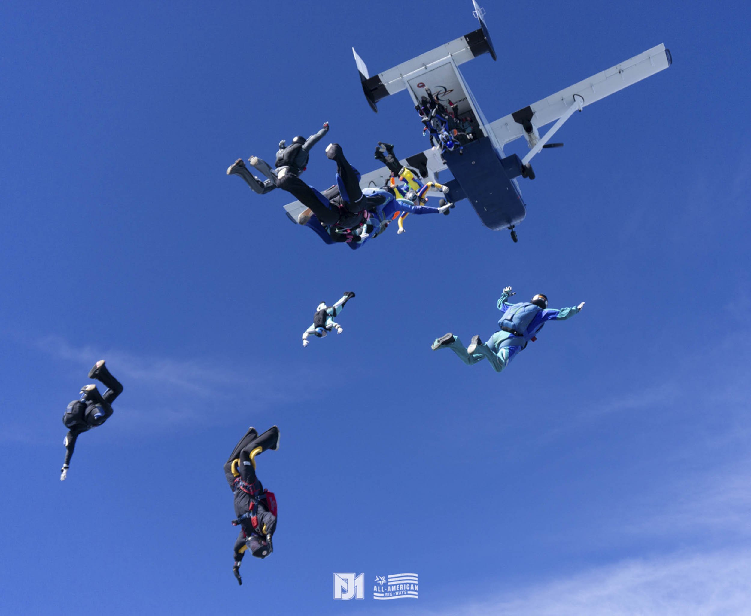 Skydivers in formation after jumping from an airplane in a clear blue sky.