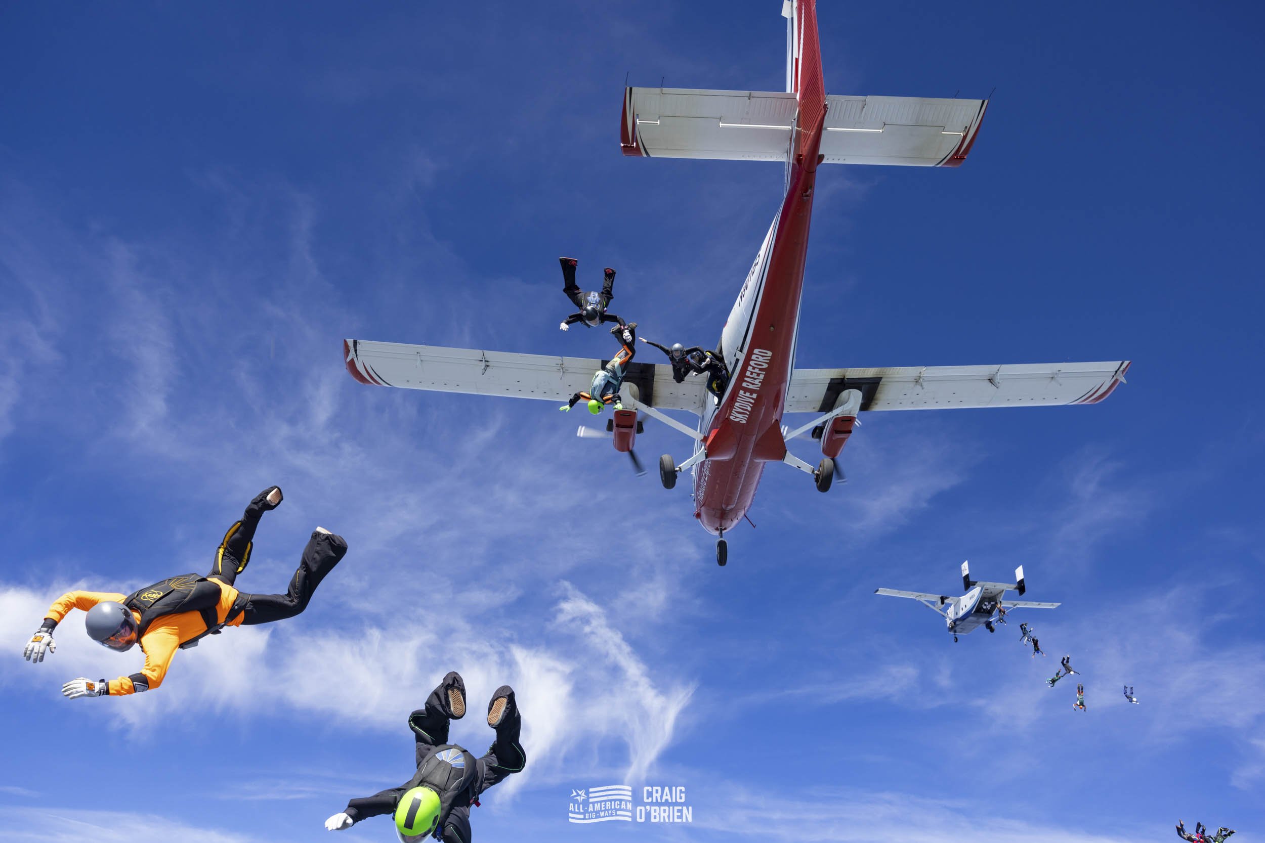 Skydivers performing a mid-air formation jump from an airplane against a blue sky with some clouds.