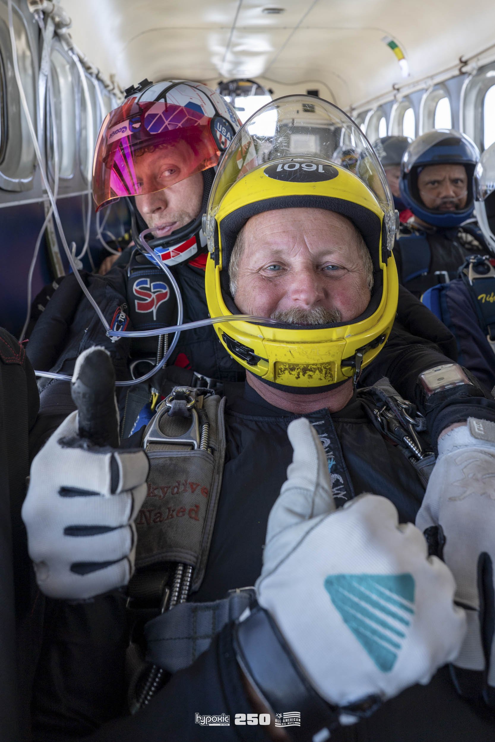 Group of airplane pilots in cockpit wearing helmets and gear, with the main pilot giving a thumbs up.