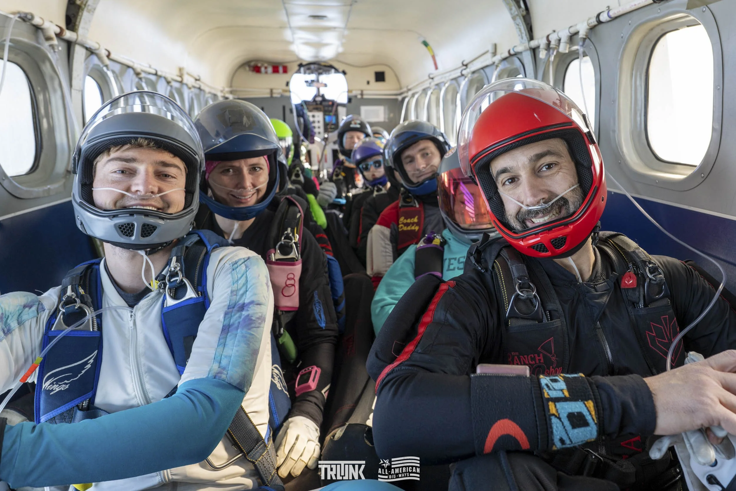 Group of skydivers inside an airplane, preparing for a jump, wearing helmets and jumpsuits.