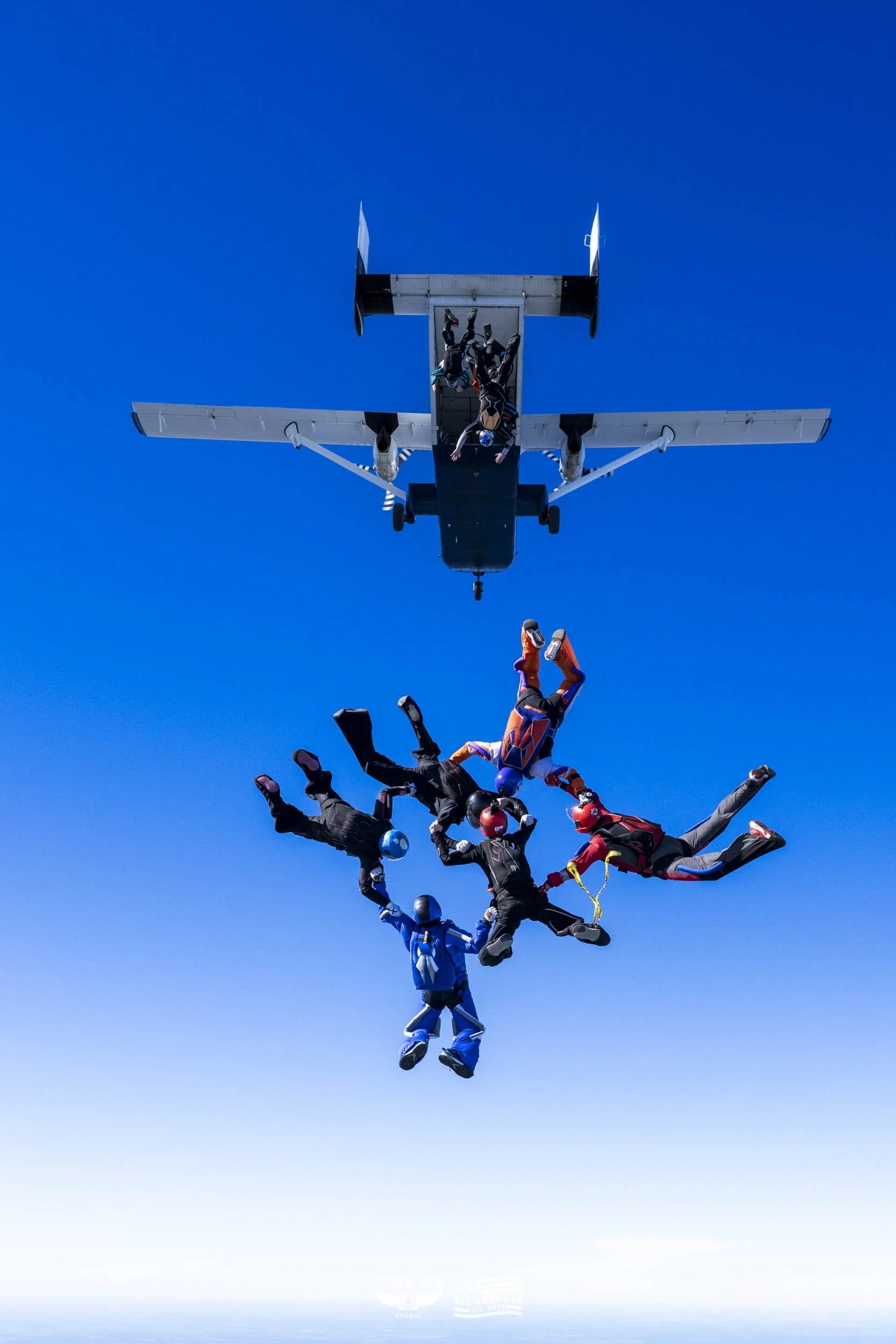 Skydivers in free fall near an airplane against a clear blue sky.