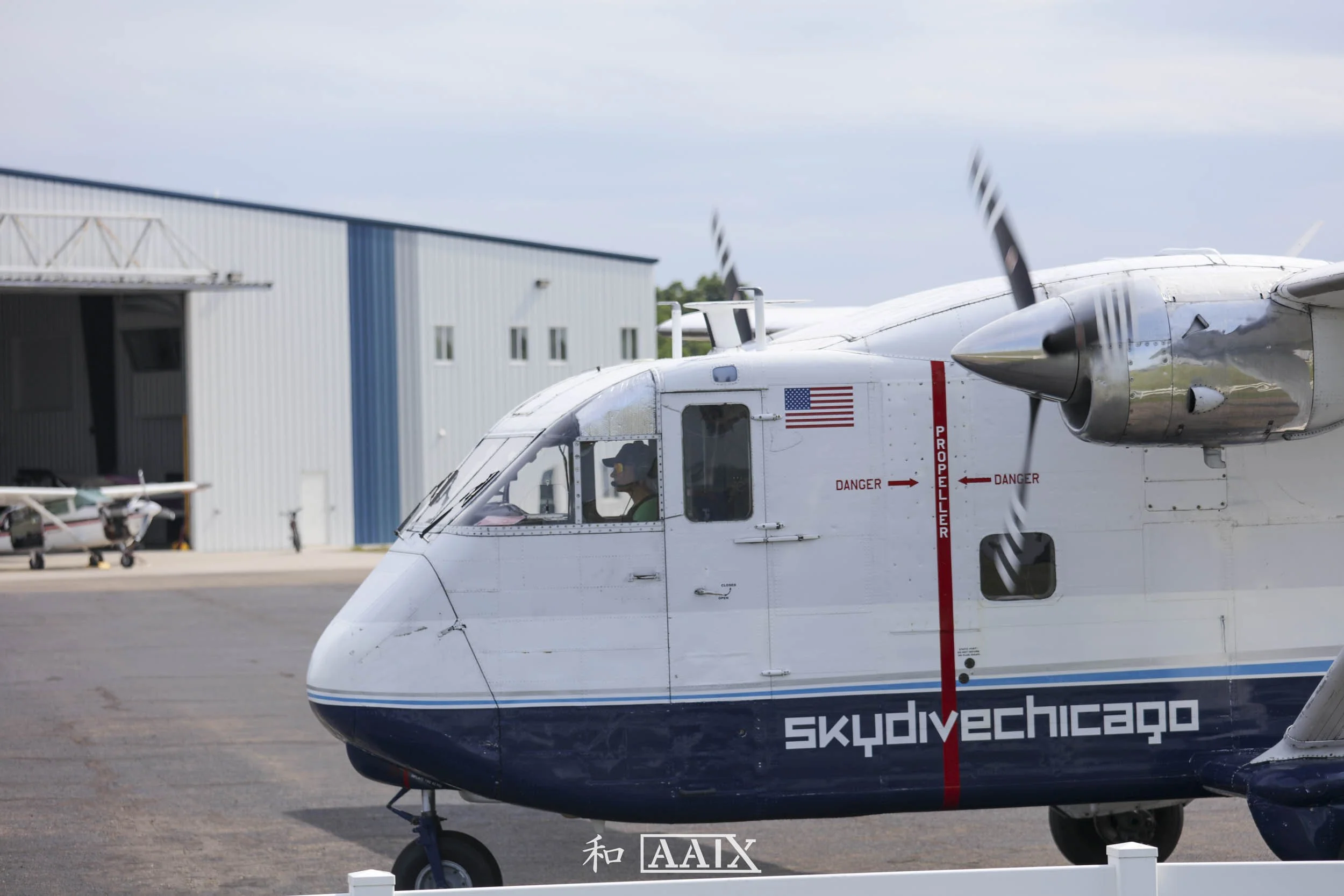 Close-up of a helicopter with the words 'skydvechicago' on the side, parked on an airstrip near a large hangar. The helicopter has propellers spinning, exuding a sense of motion.