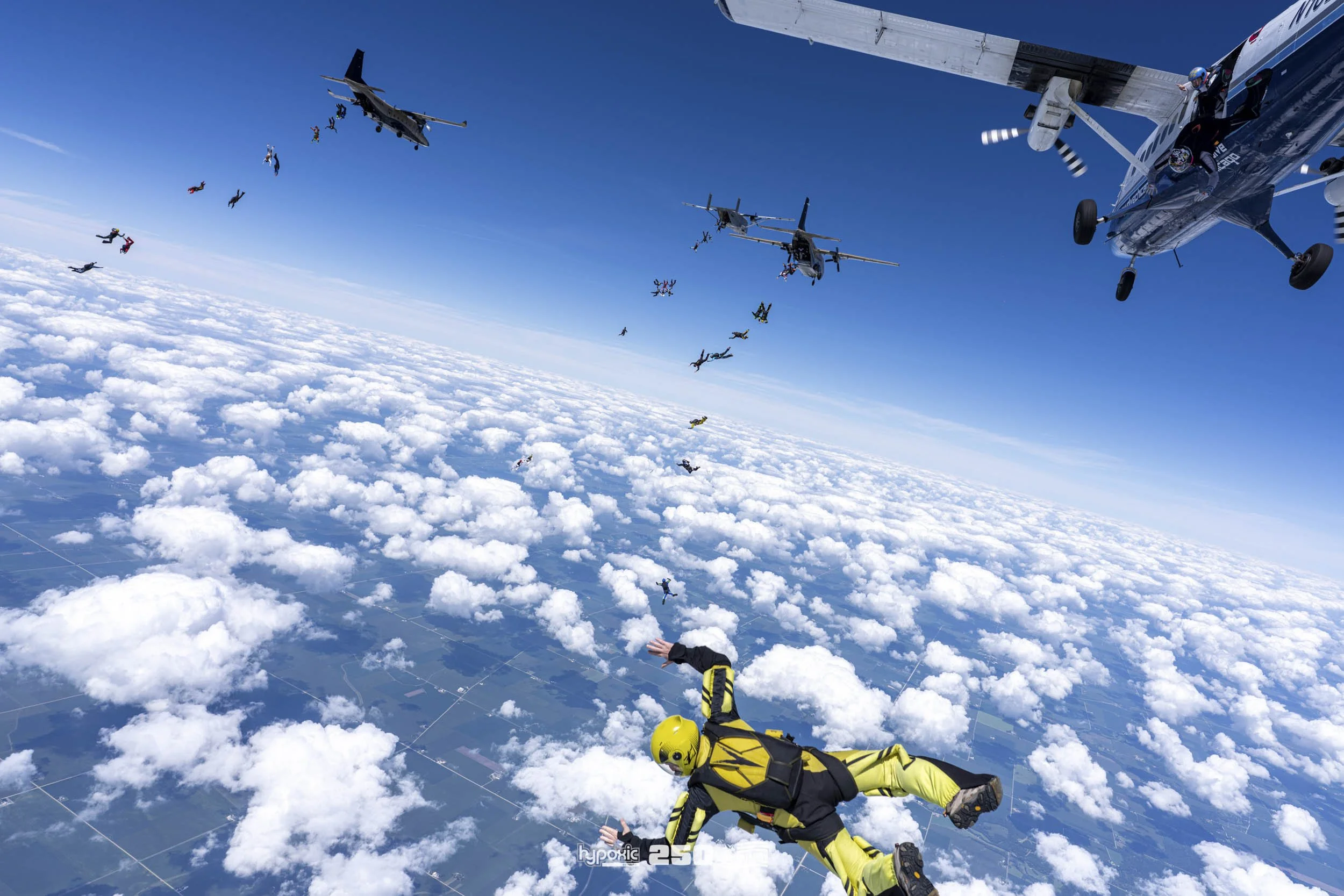 Skydivers jumping from a plane high above the clouds.