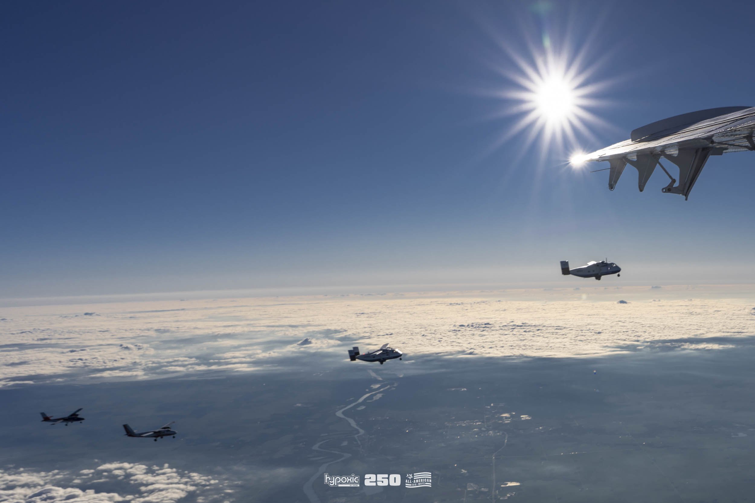 Military aircraft flying high above the clouds in clear weather, with the sun shining brightly in the sky.