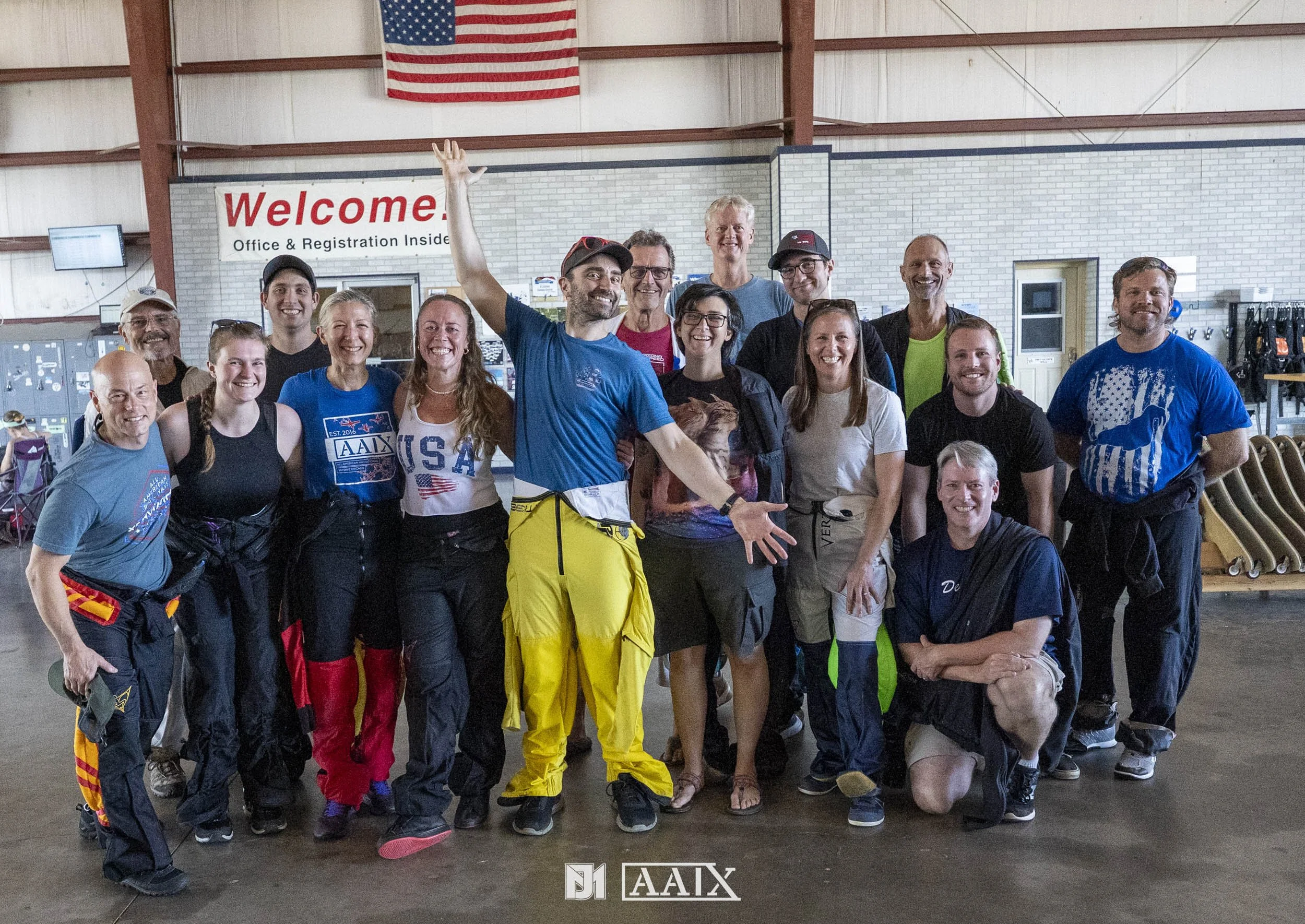 Group of 16 people smiling together inside a building, posing for a photo, with a 