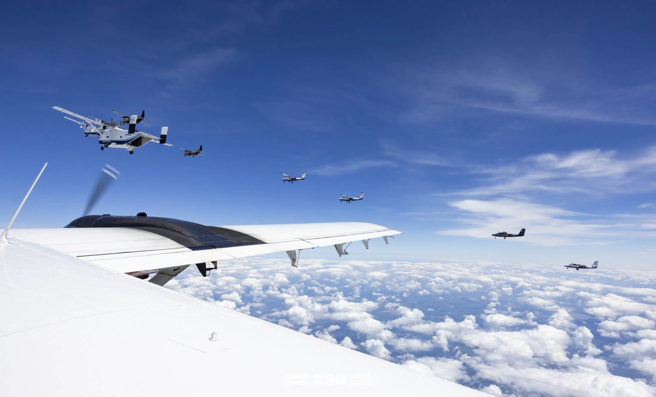 Several aircraft flying in formation above clouds in the sky, including a large drone or aircraft in the foreground and smaller planes in the background.