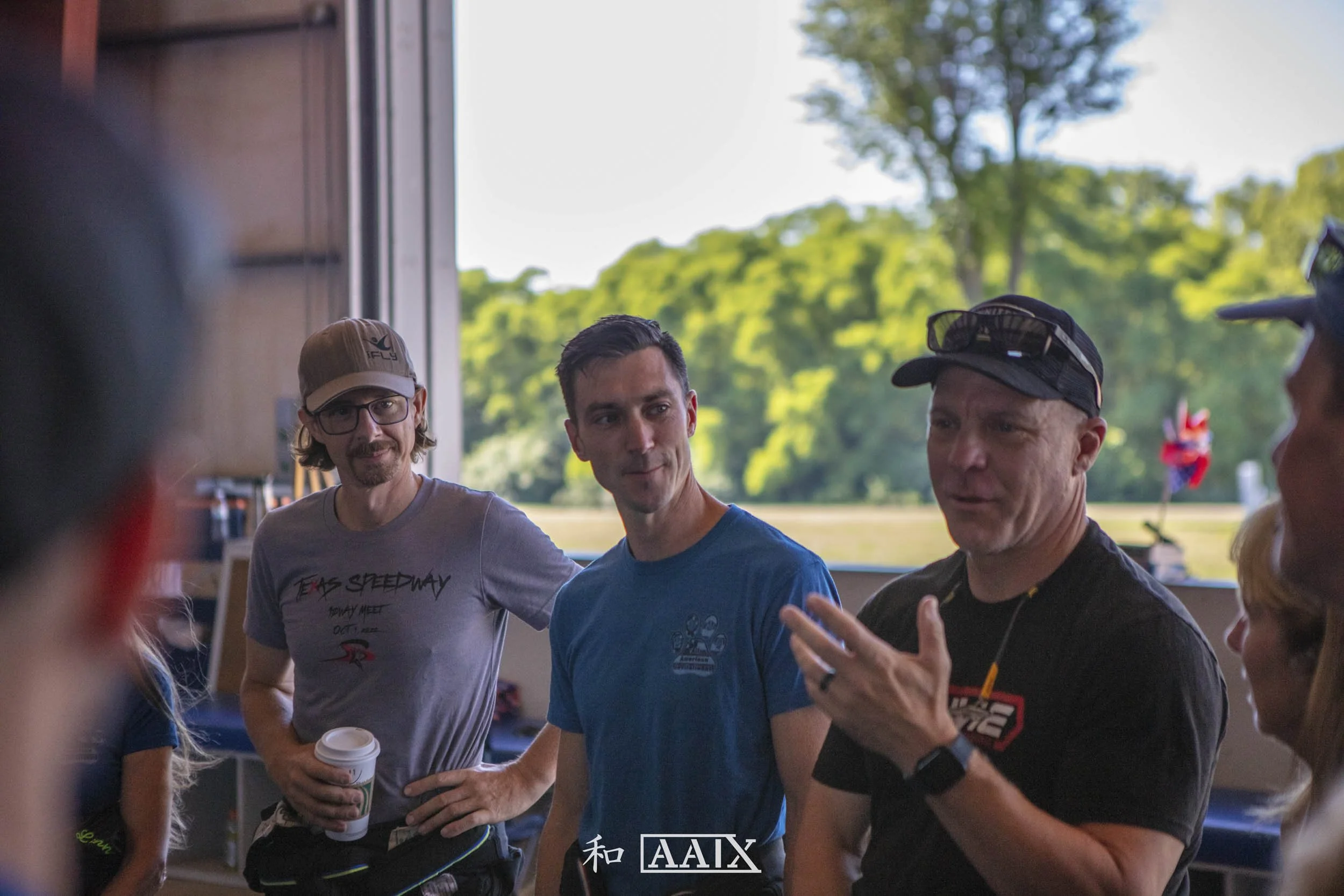 Group of people indoors, engaging in conversation, with a scenic view of trees through a window.