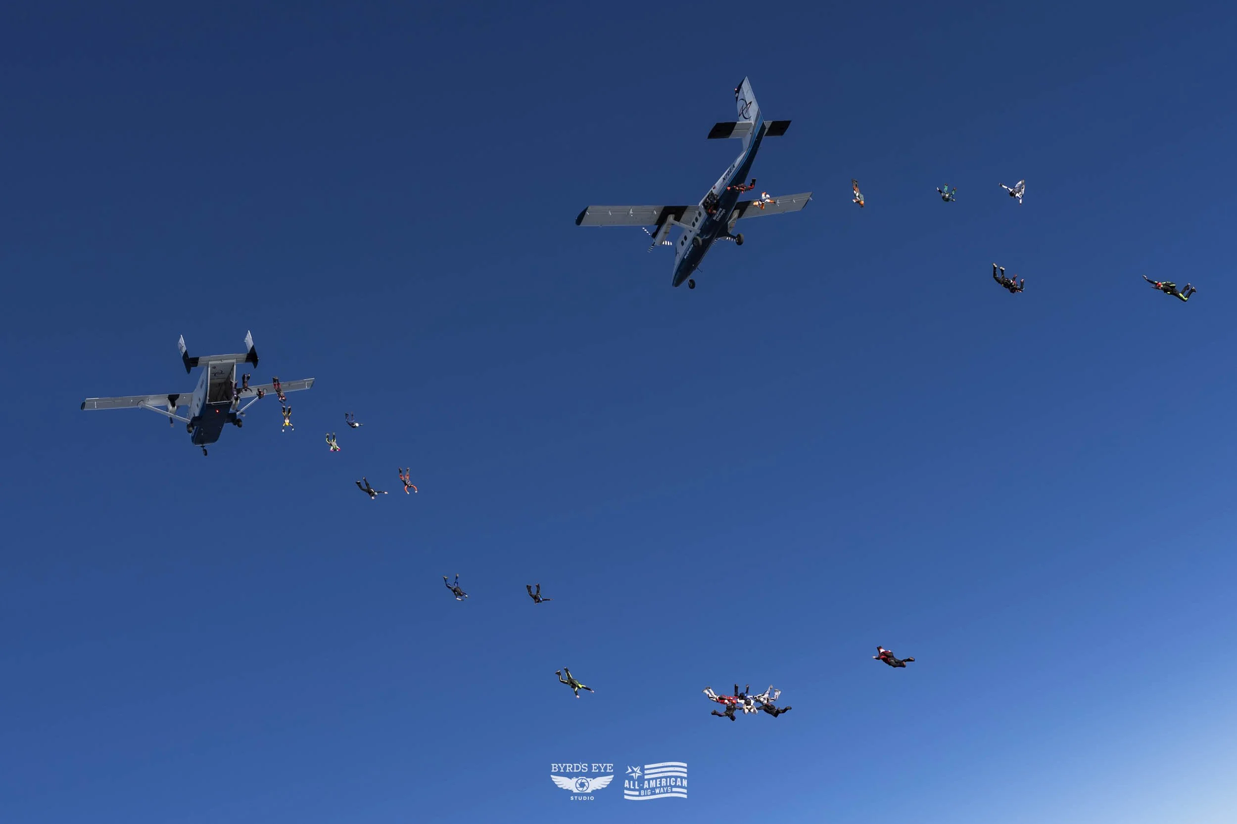 Two aircrafts flying in the sky with numerous skydivers jumping from both planes.