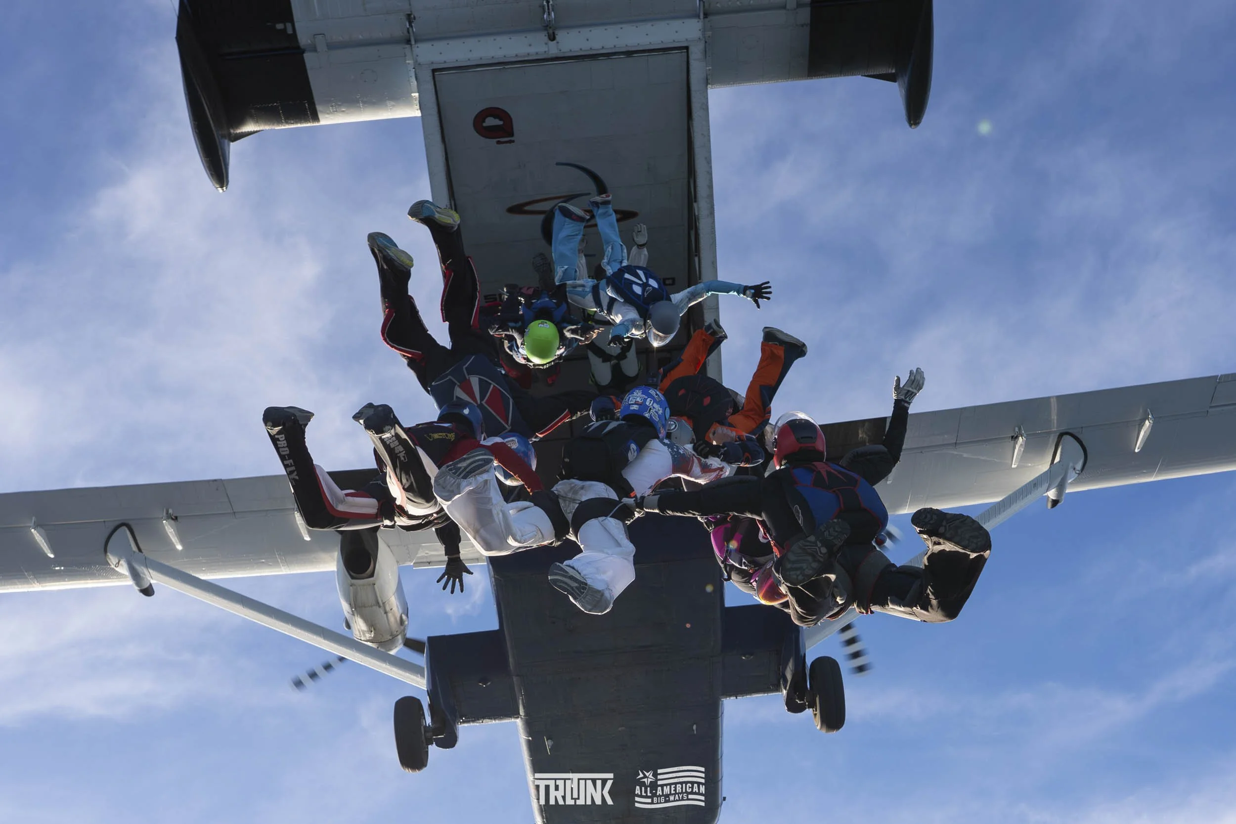A group of skydivers in freefall formation after jumping from an aircraft, with the open sky in the background.