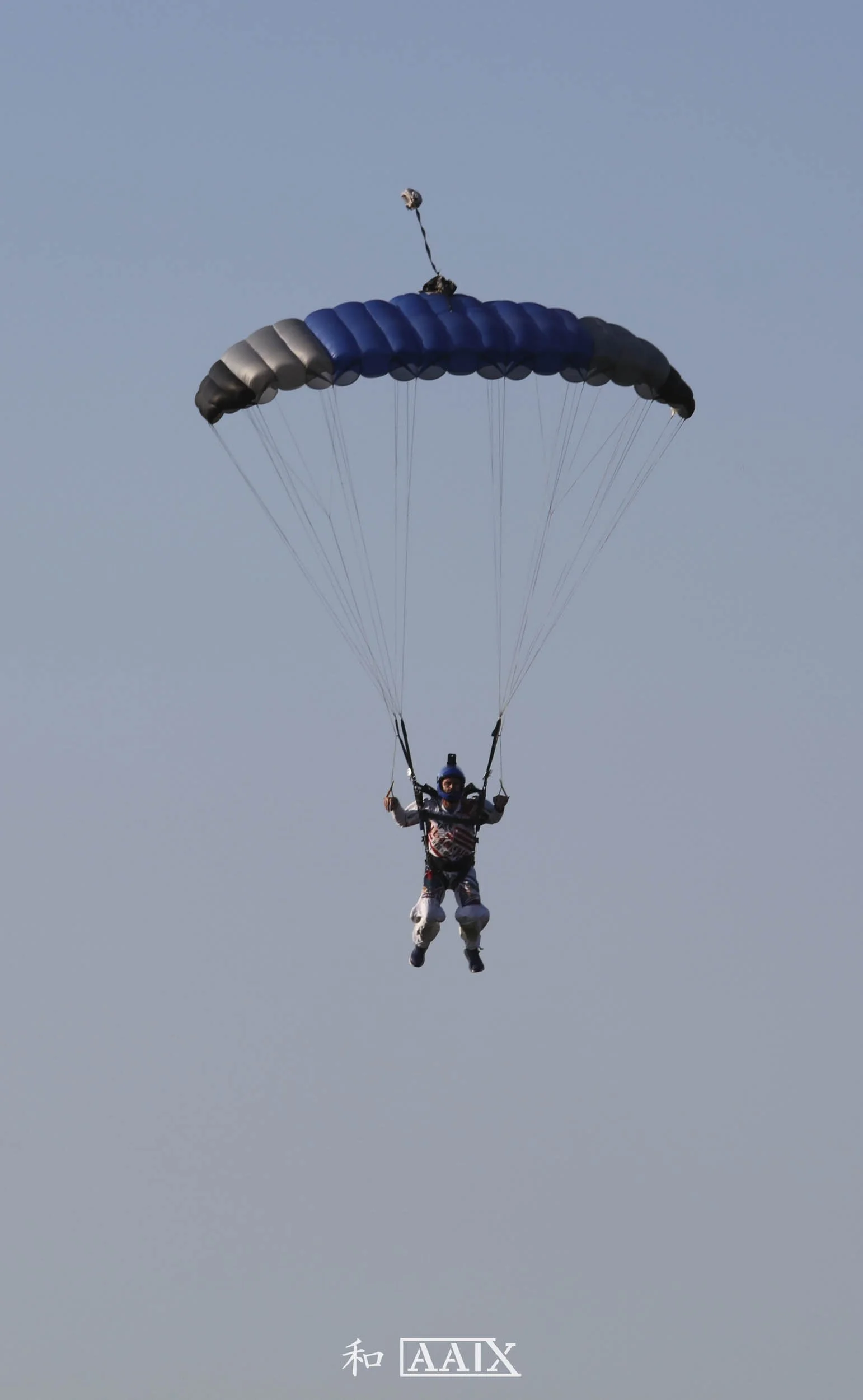 A person skydiving with a blue and gray parachute in a clear sky.