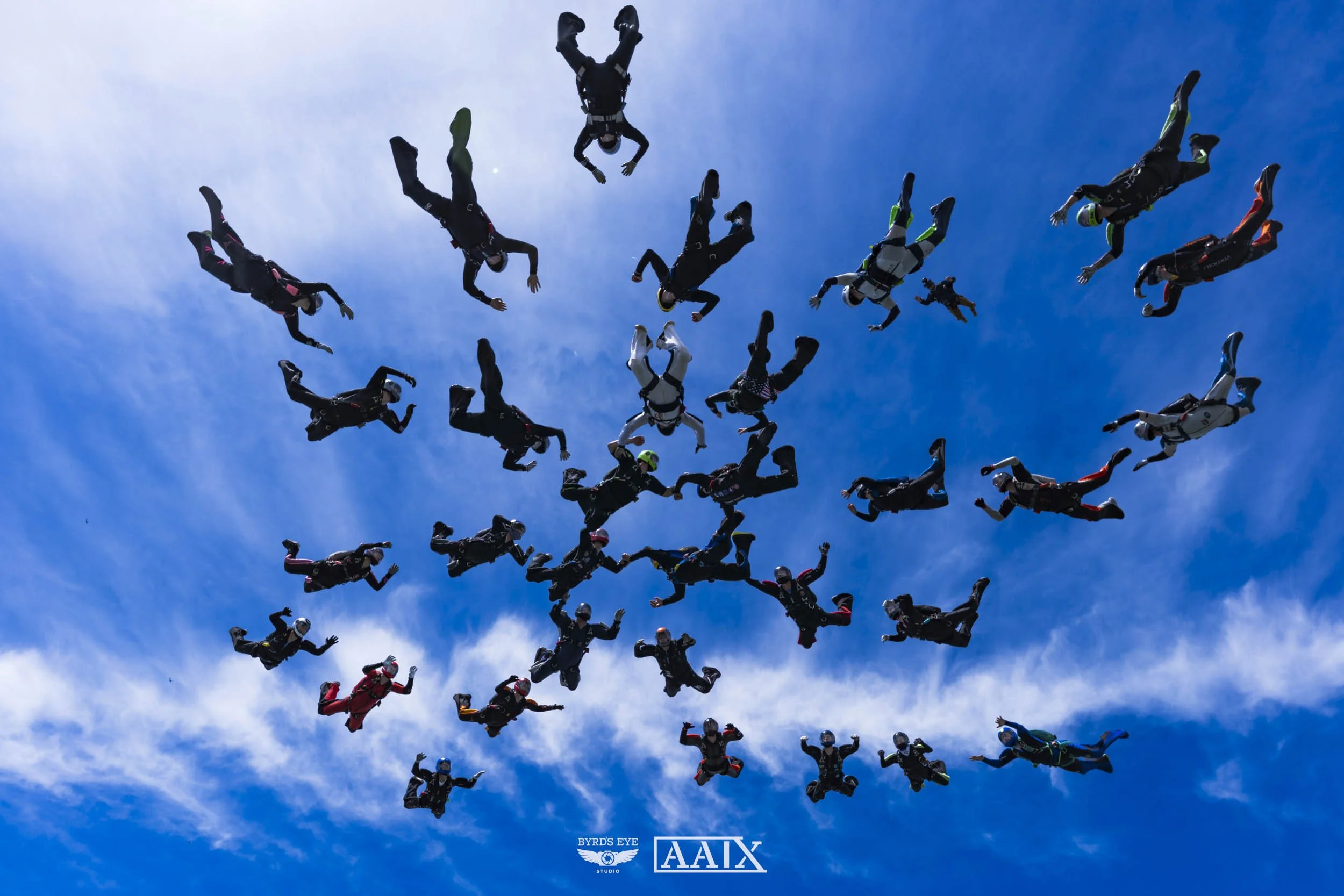 Group of skydivers in free fall against a blue sky with scattered clouds.