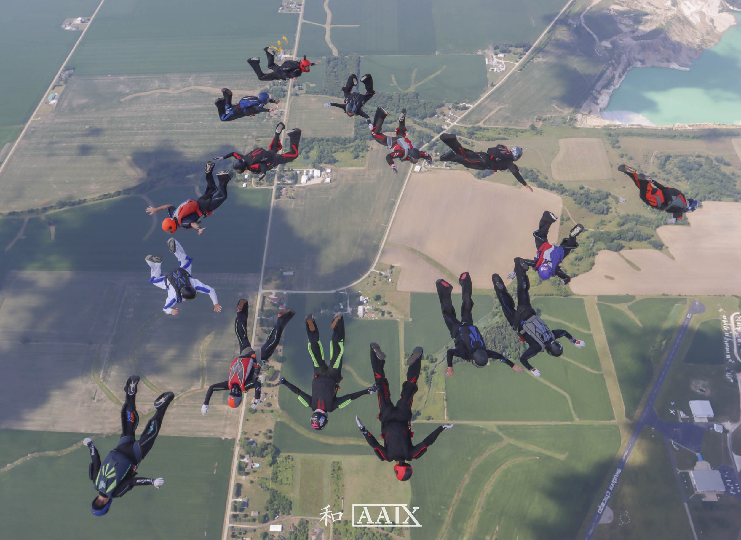 Group of skydivers free-falling over rural farmland and a lake in daytime.