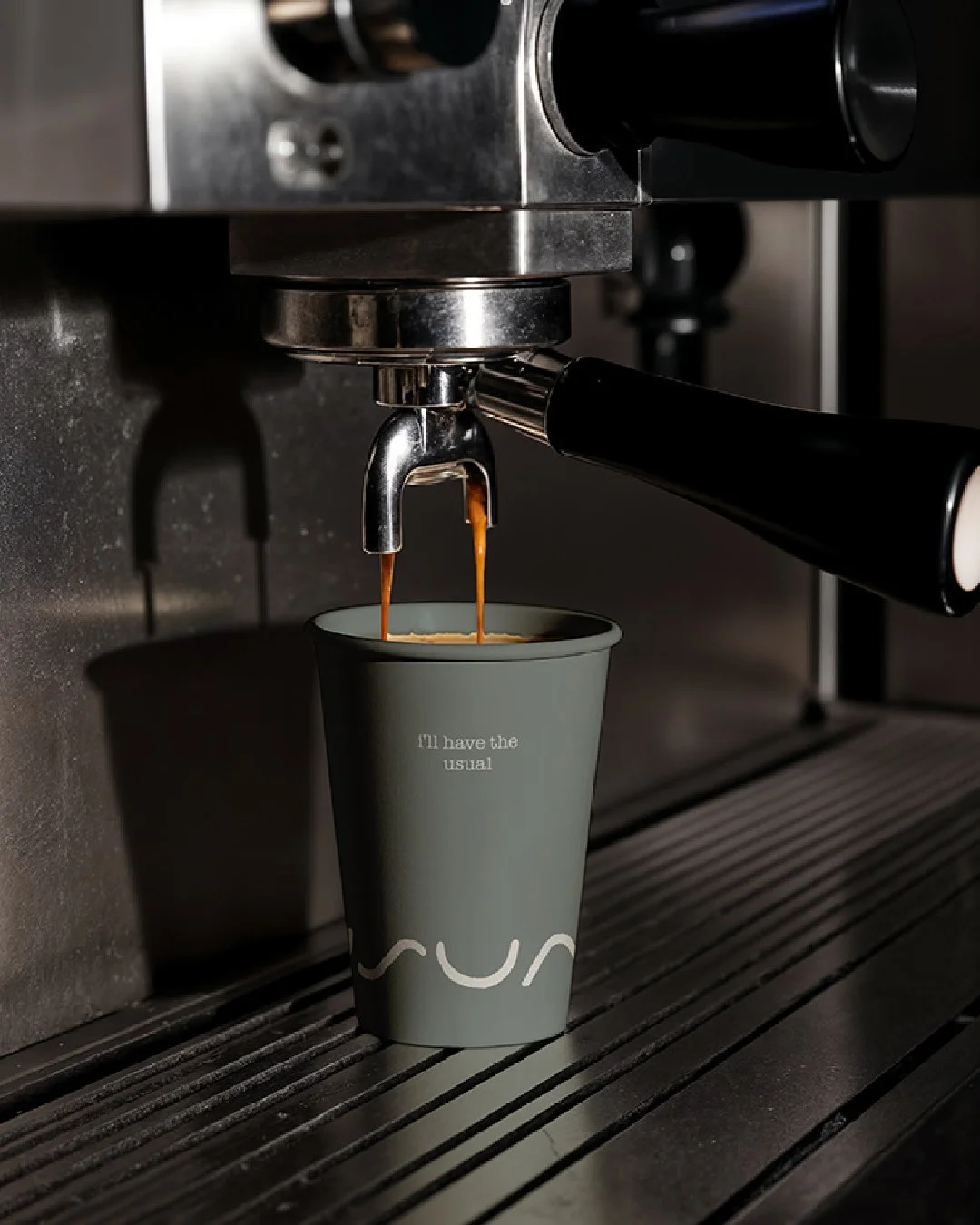 Espresso pouring into a takeaway coffee cup branded ‘The Usual’ on a café coffee machine.