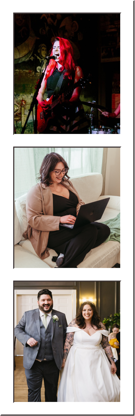 A woman with long red hair singing and playing guitar on stage, with a microphone in front of her and a drummer behind her. She appears to be performing in a music venue with artwork on the wall in the background.