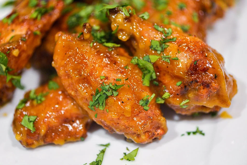 Close-up of spicy buffalo chicken wings garnished with chopped parsley on a white plate.