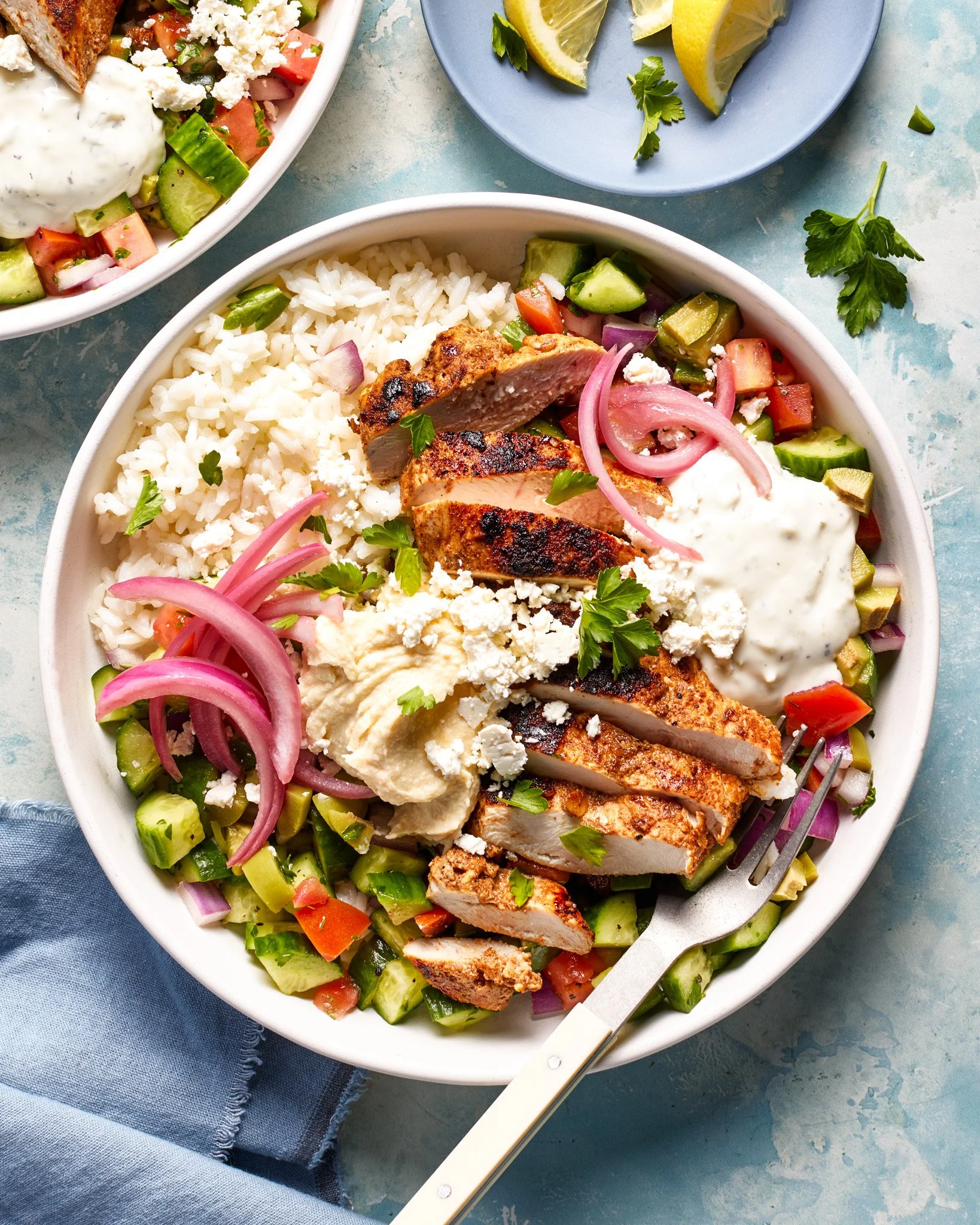 Chicken shawarma salad with chopped cucumber, tomato, red onion, and parsley, topped with hummus and feta cheese, served in a bowl with a fork.