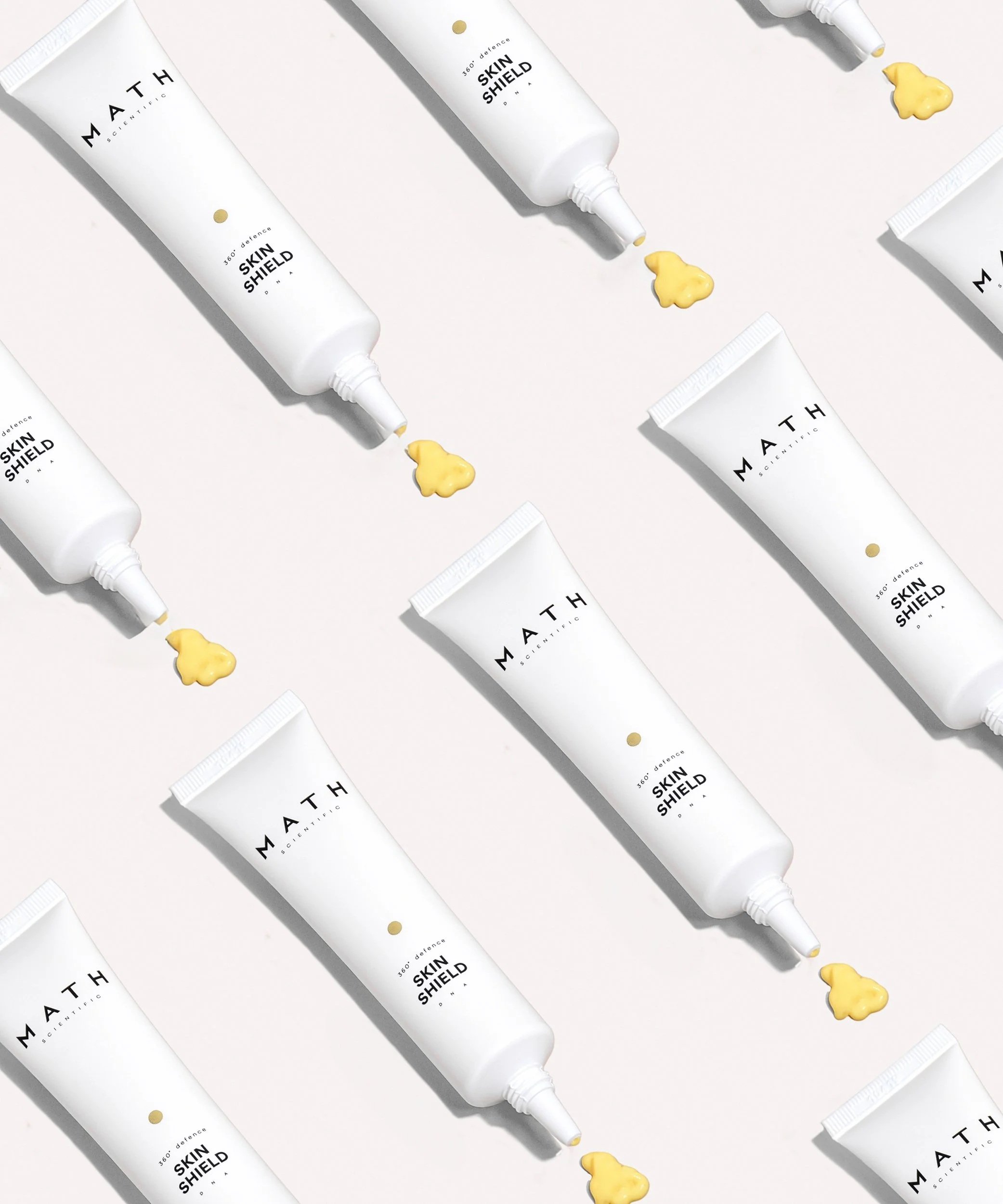 Multiple tubes of skin care product labeled 'Math Scientific Skin Shield' arranged on a white surface, with yellow cream or gel squeezed out from the nozzle of some tubes.