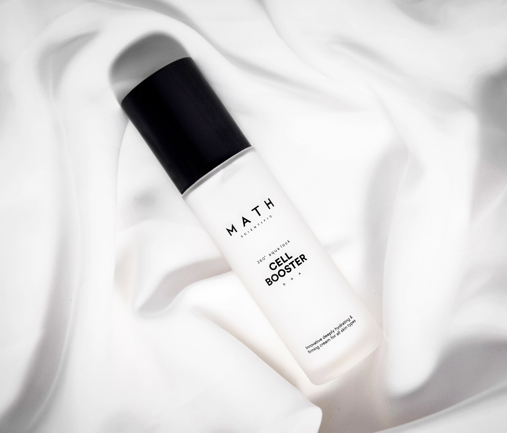 Close-up of a white skincare product tube with black cap on white fabric. 
