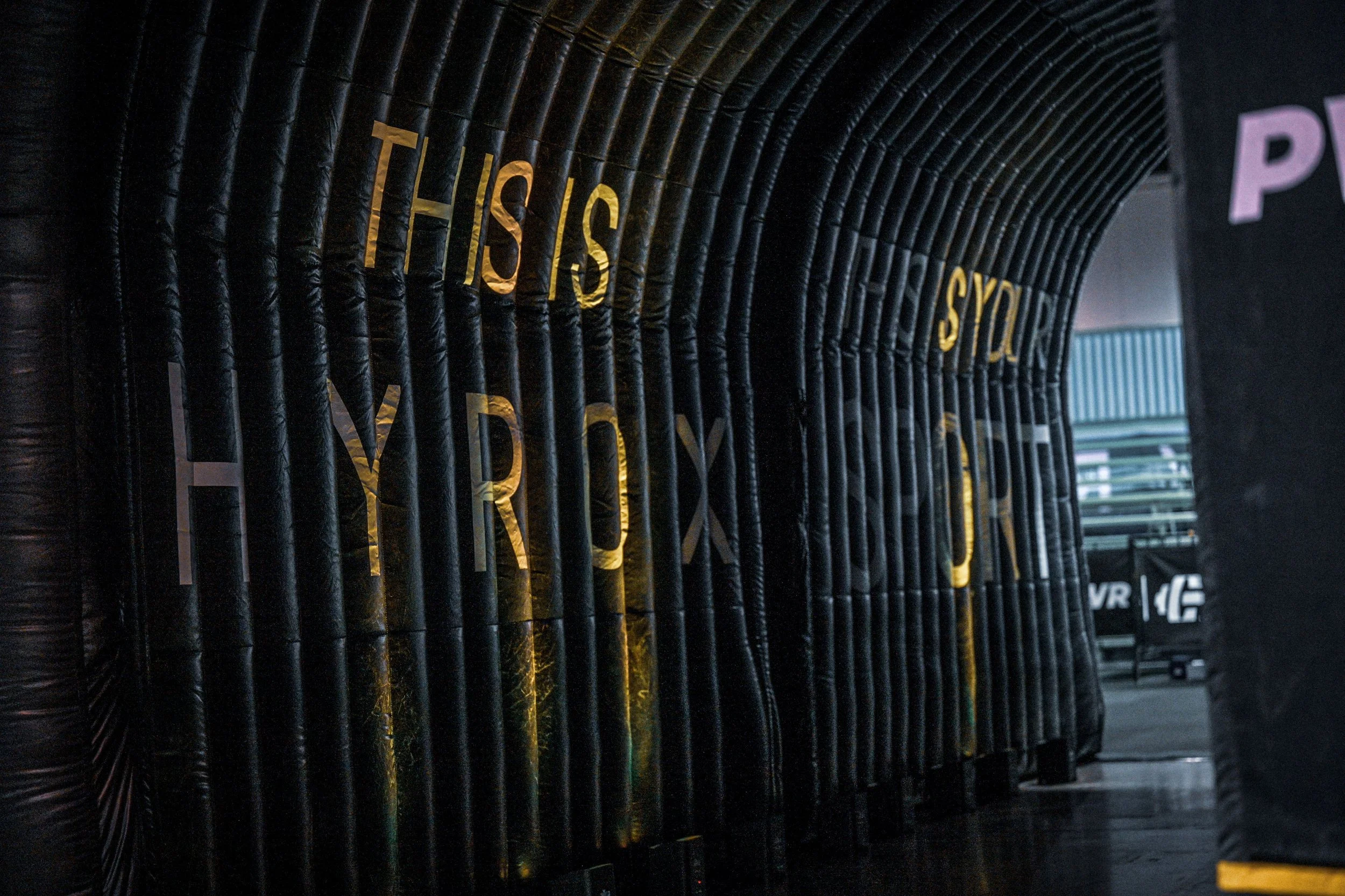 An inflatable black structure with a series of tubes, with gold-lettered text saying 'THIS IS YOUR BOX' on it.