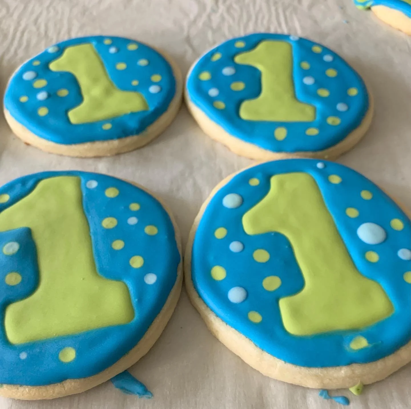 Cookies decorated with blue icing and yellow-green number 1, with yellow and white dots for celebration.