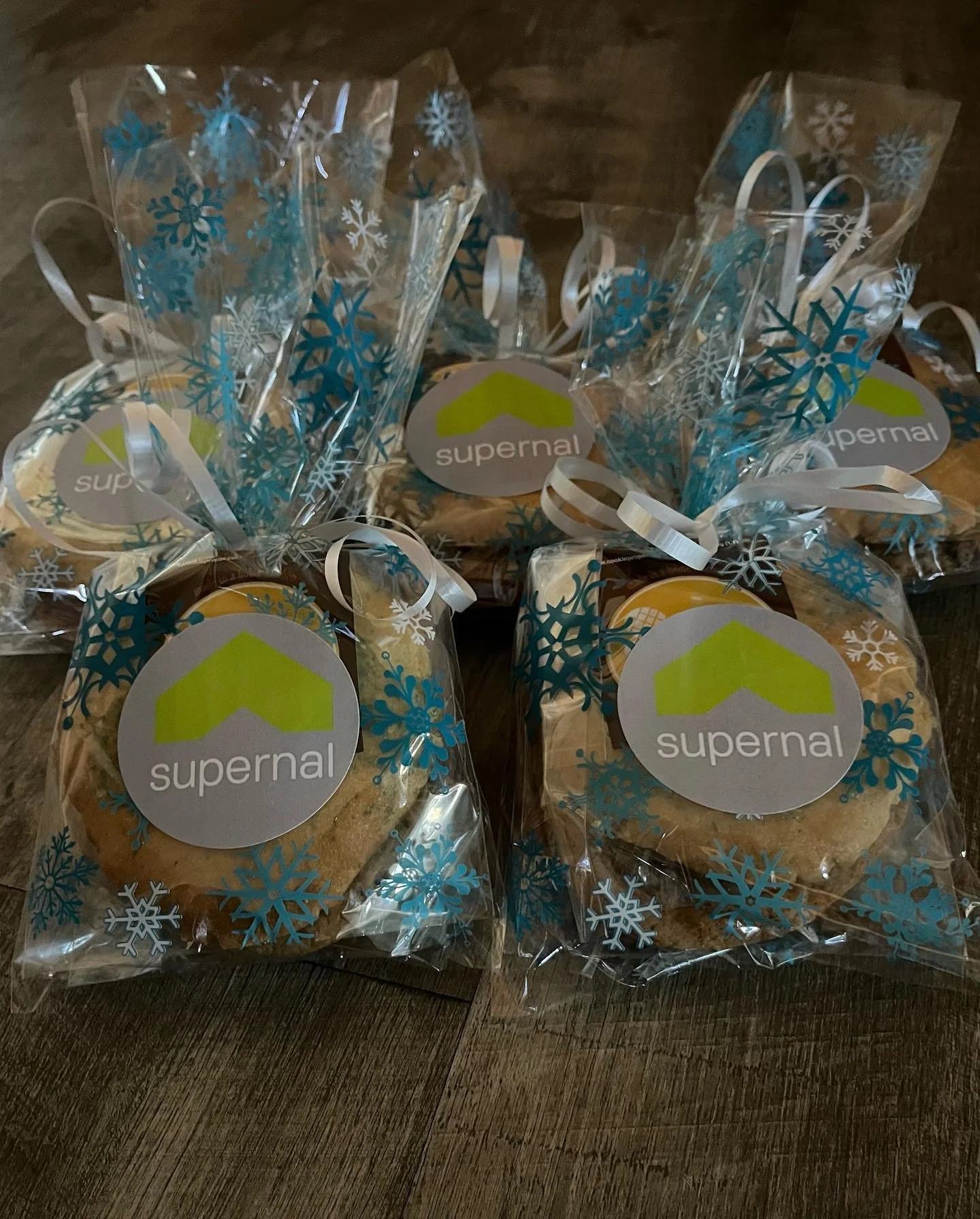 Gift bags decorated with snowflakes and a 'supernal' logo, containing cookies, on a wooden surface.