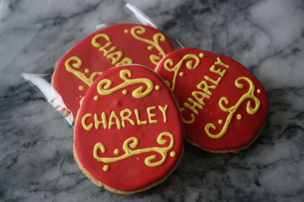 Round cookies with red icing decorated with yellow icing, spelling 'Charley's' and some decorative swirls.