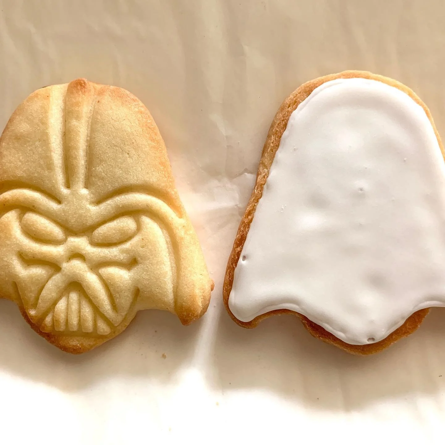 Star Wars-themed cookie shaped like Darth Vader's helmet next to a ghost-shaped sugar cookie with white icing.