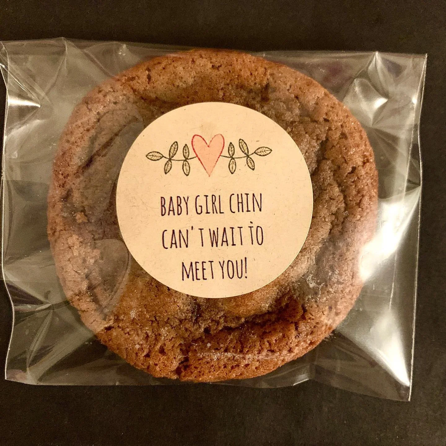 Close-up of a wrapped cookie with a label that reads 'Baby girl chin can't wait to meet you!'