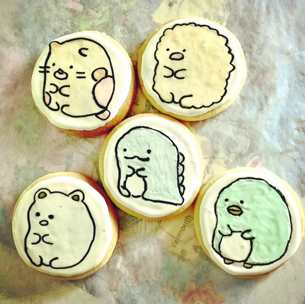 Five decorated cookies featuring cartoon-style drawings of various animals, including a bear, a bird, a chick, a dinosaur, and a hamster. Each cookie has a white icing background with black outlines and simple facial features.