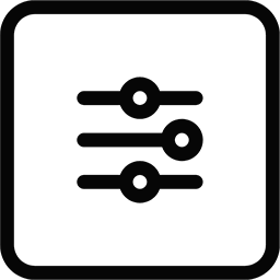 A black dog lying down on a gray surface, looking towards the camera.