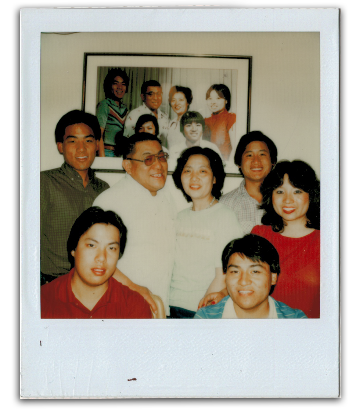 A group of eleven people posing for a photo in front of a wall, with a smaller framed photo of the same group in the background.