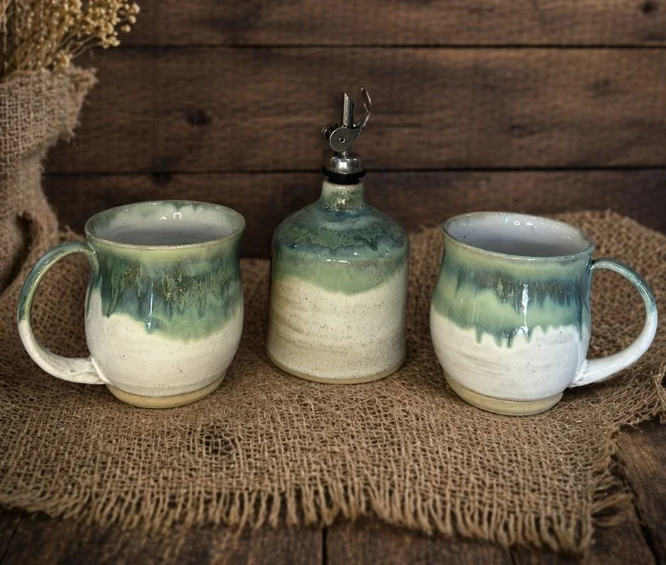 Two ceramic coffee mugs and a ceramic bottle with a pour spout, all with green and white glaze,