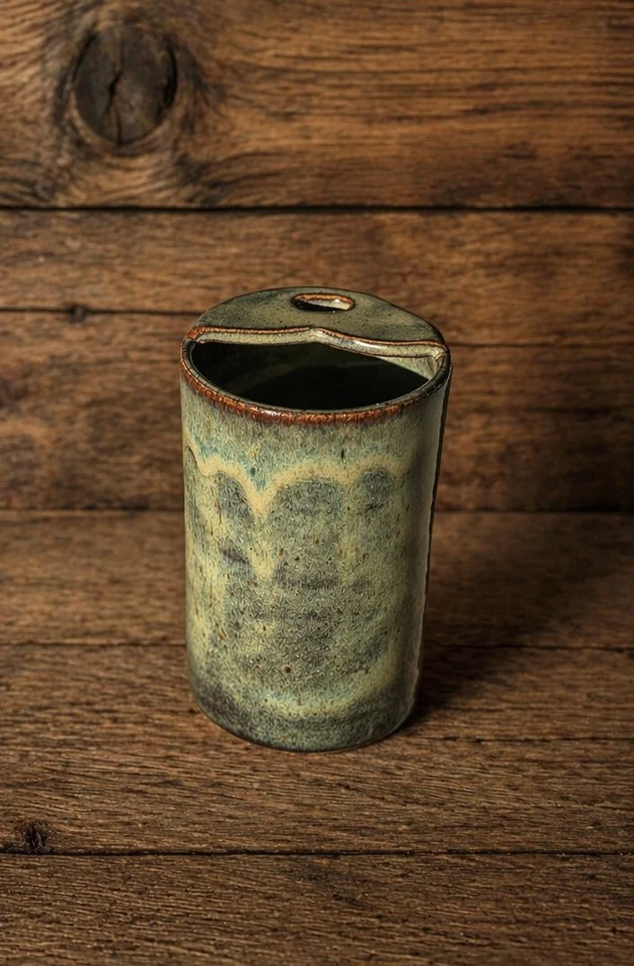 A ceramic travel mug with a textured, glazed surface in shades of green and brown, 