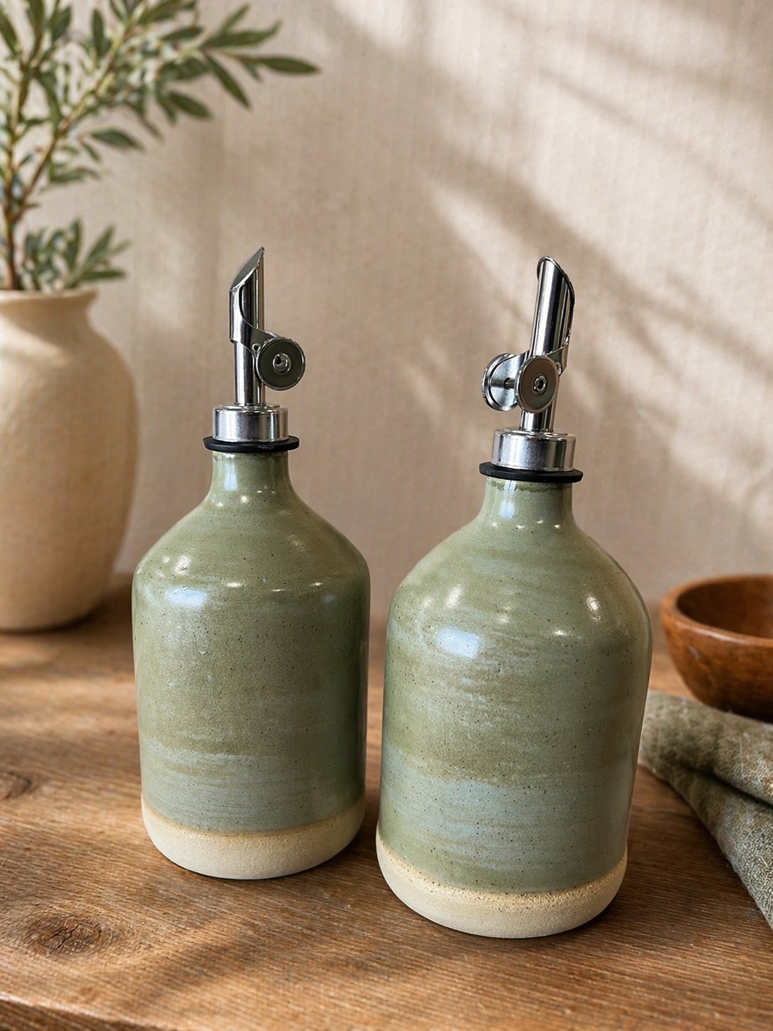 Two ceramic oil bottles with metallic pour spouts.