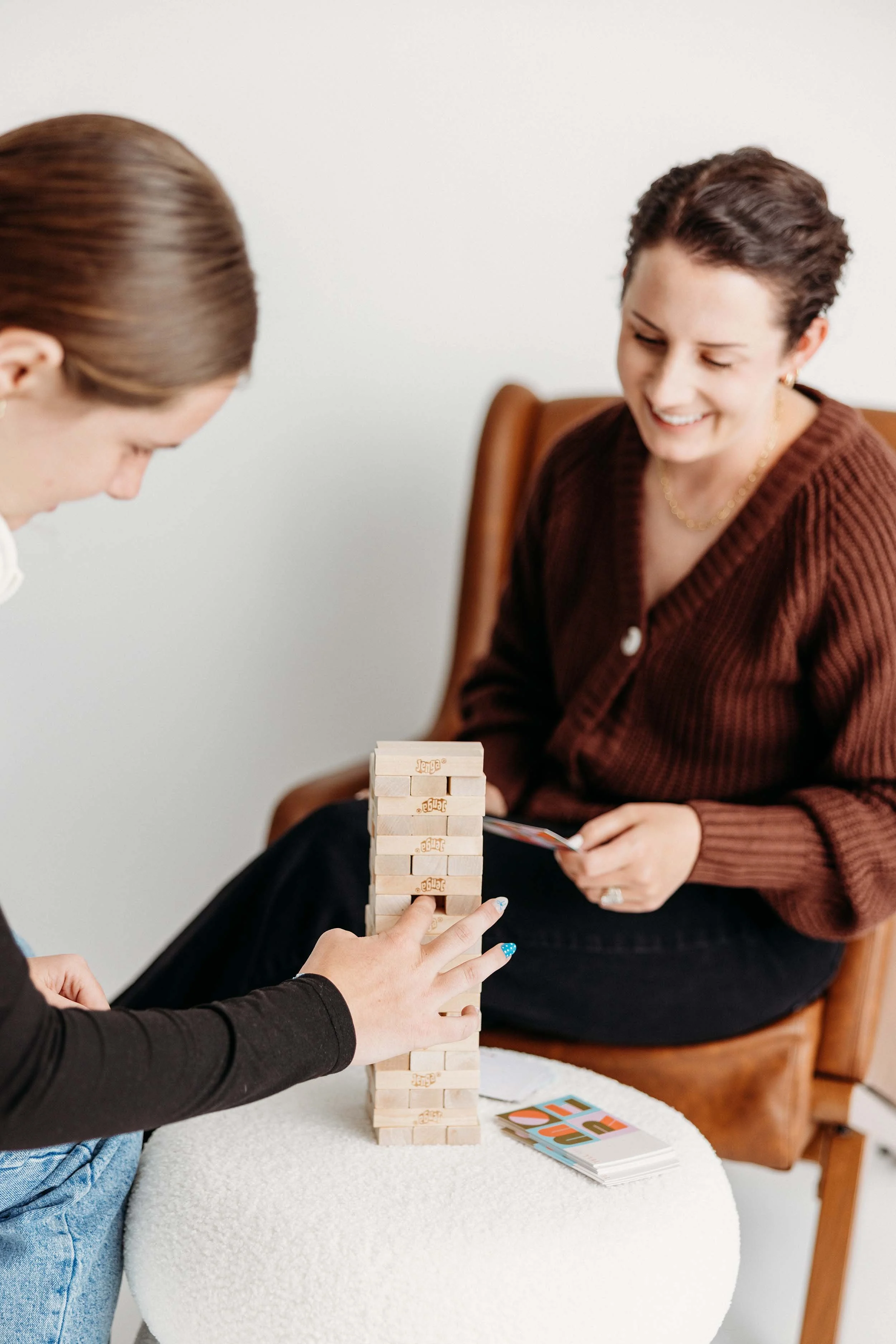 Two women playing Jenga and cards at a table.