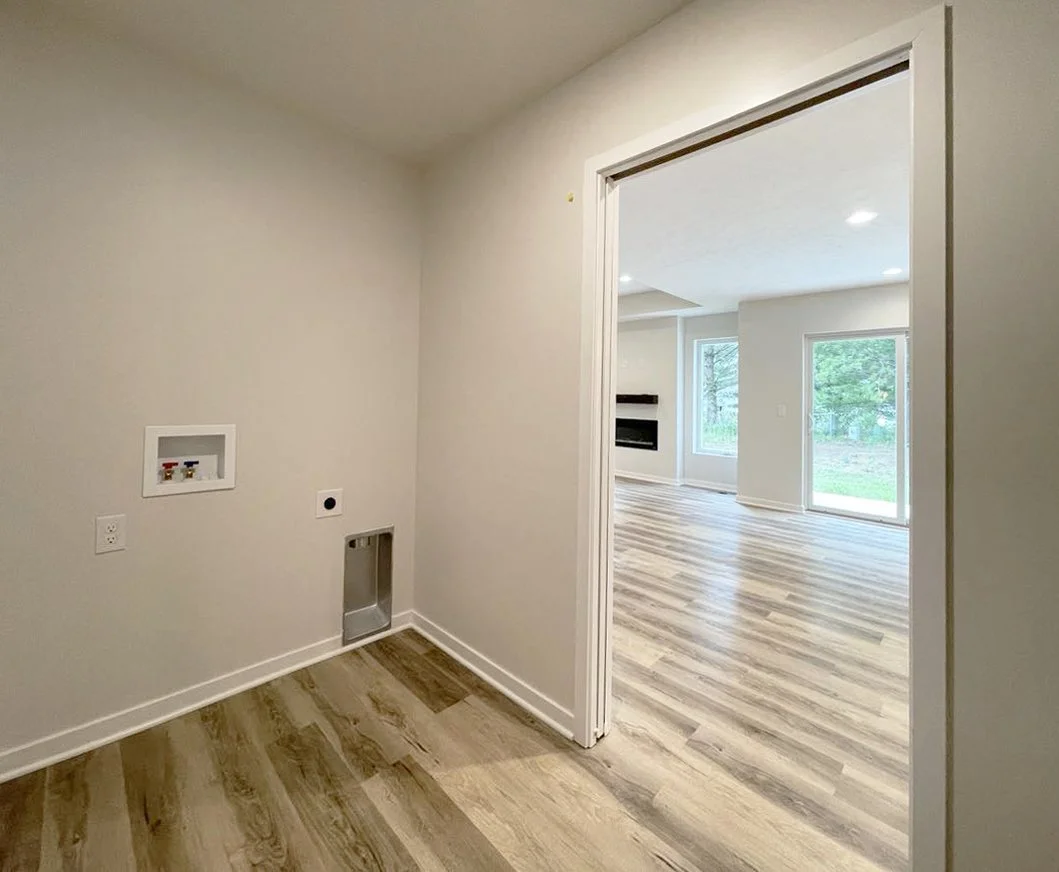 A laundry room with hookups and vent, opening into a bright living room with wood flooring and large windows.