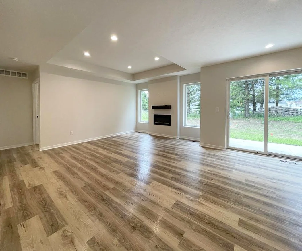 A living room with light wood floors, white walls, a fireplace, several windows, and a sliding glass door leading outside.