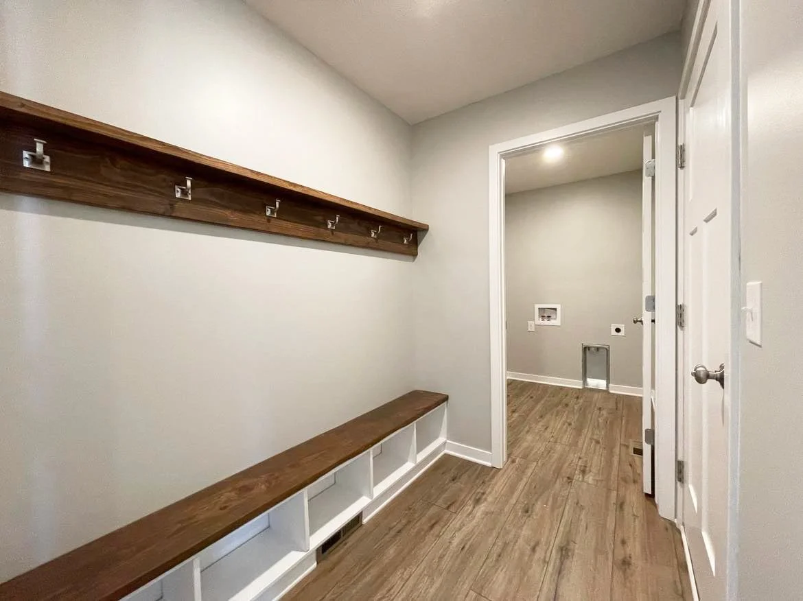 A laundry room and mud room with wooden bench and coat hooks on the wall.