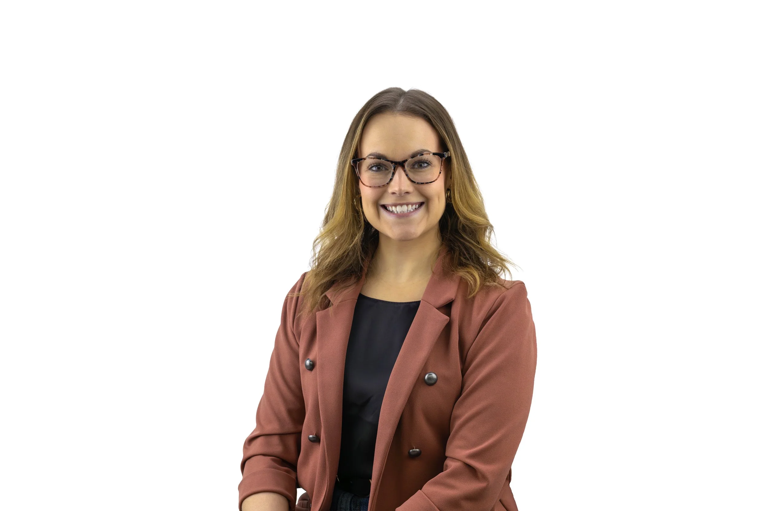 A woman with long wavy hair, wearing glasses, a black top, and a tan blazer, smiling against a white background.